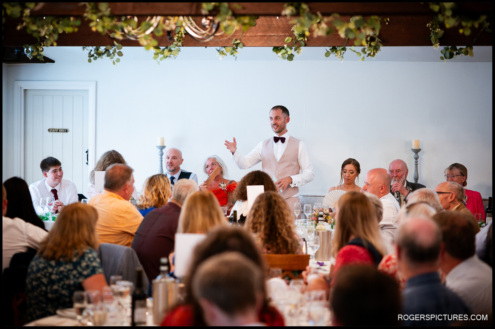 Groom giving a speech at the top table while guests listen and laugh.