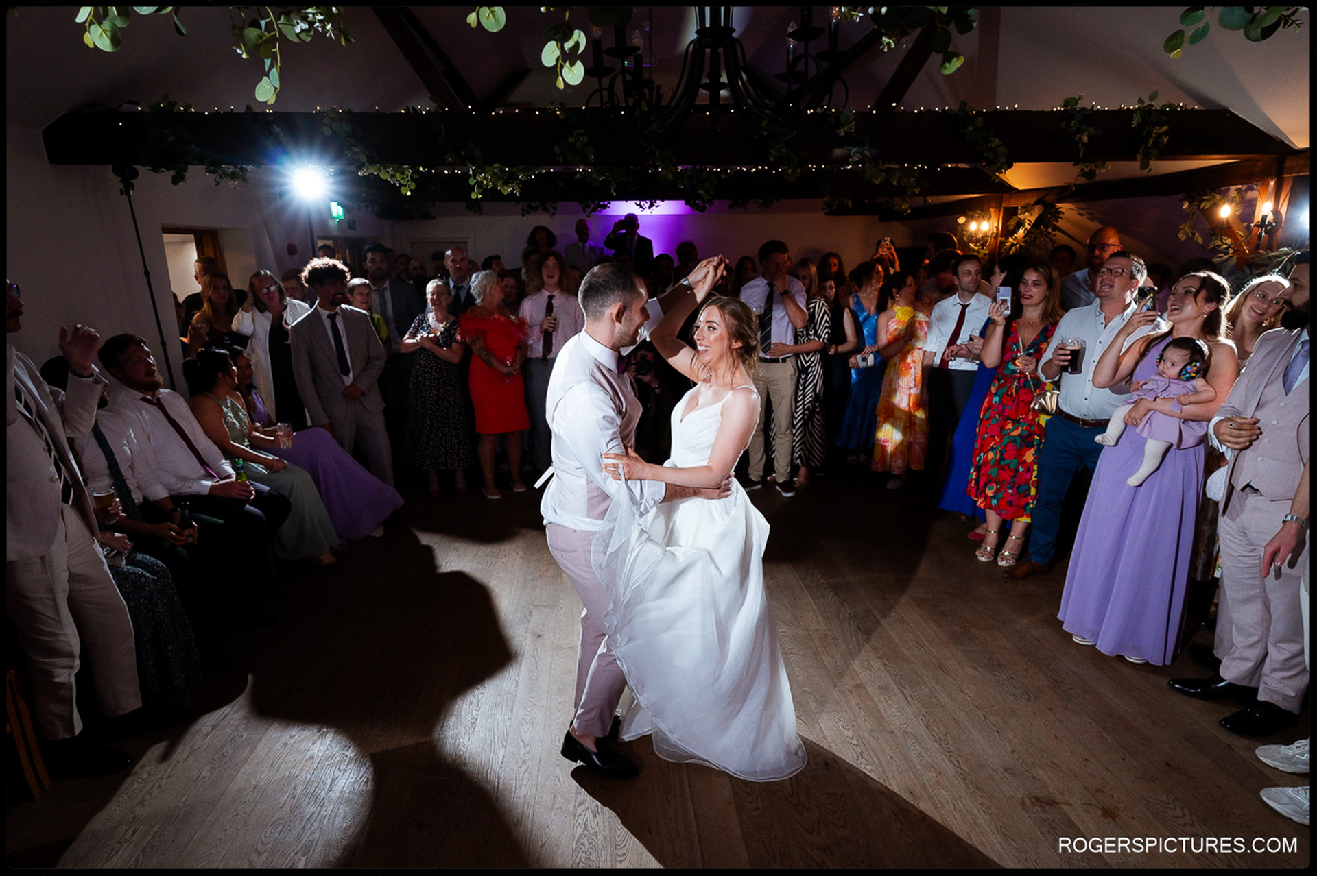 Couple twirling during first dance as guests watch and film on their phones.