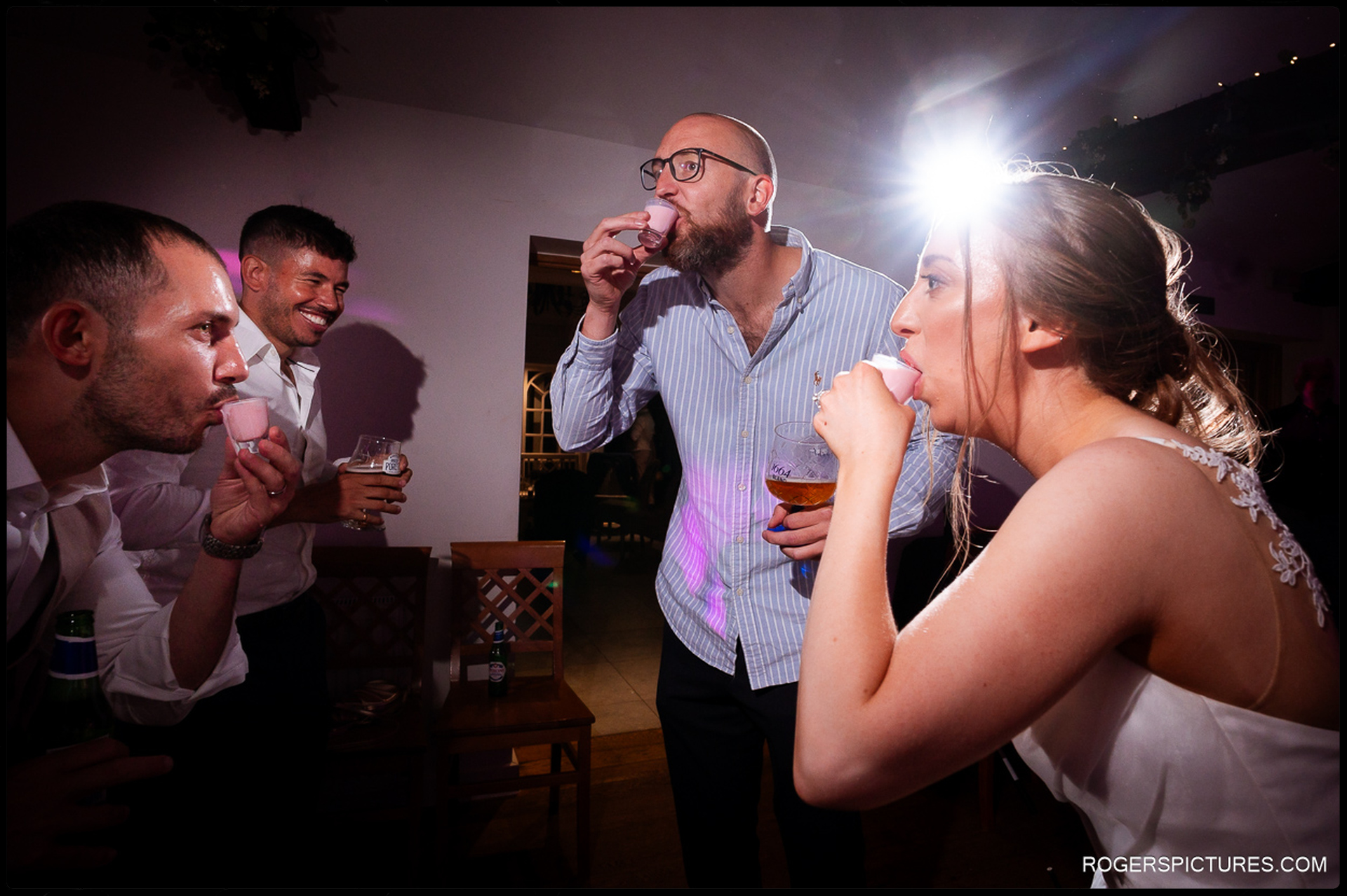 Bride, groom and guests doing pink shots together during the wedding party