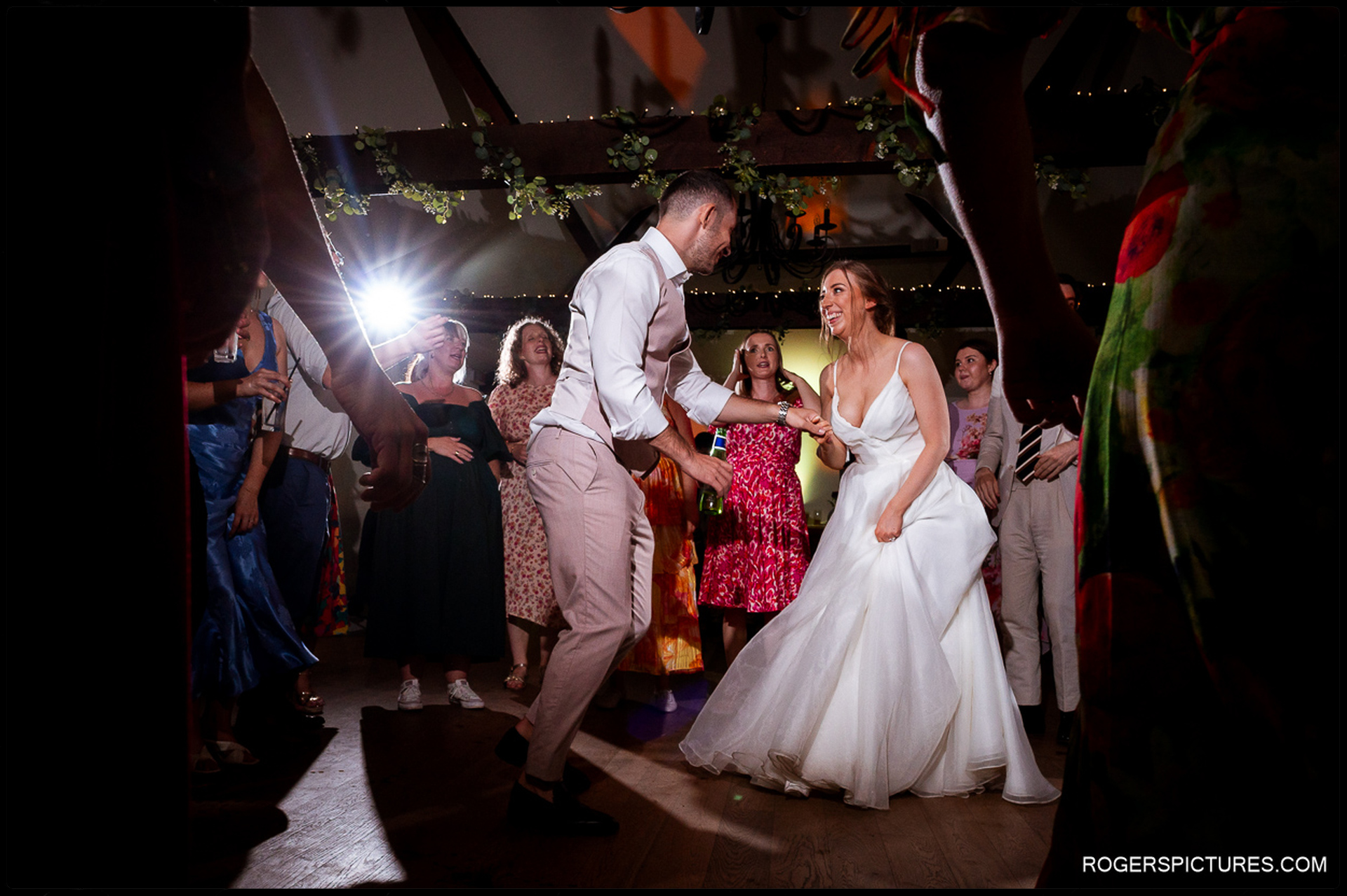Bride and groom dancing surrounded by guests under spotlights on the dancefloor