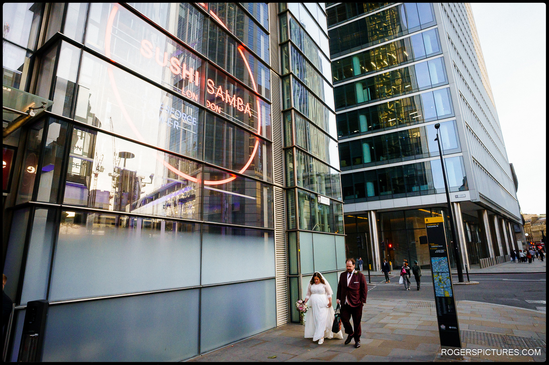 Bride and groom walk towards the SushiSamba entrance in London’s financial district, modern skyscrapers reflecting the city around them.