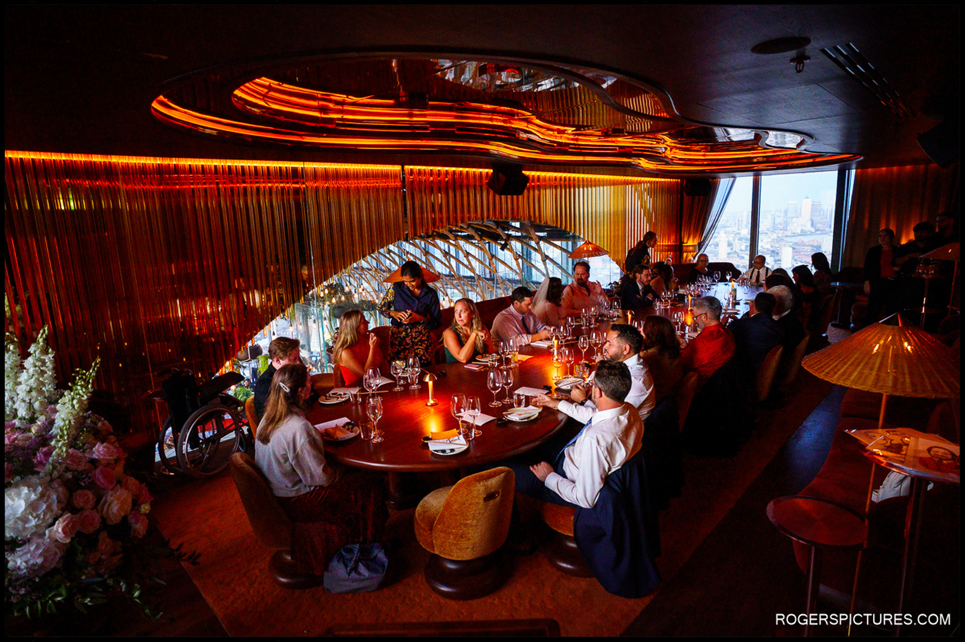 Guests seated around a large table at SushiSamba for the wedding dinner, warm candlelight and dramatic architectural lighting overlooking the London skyline.