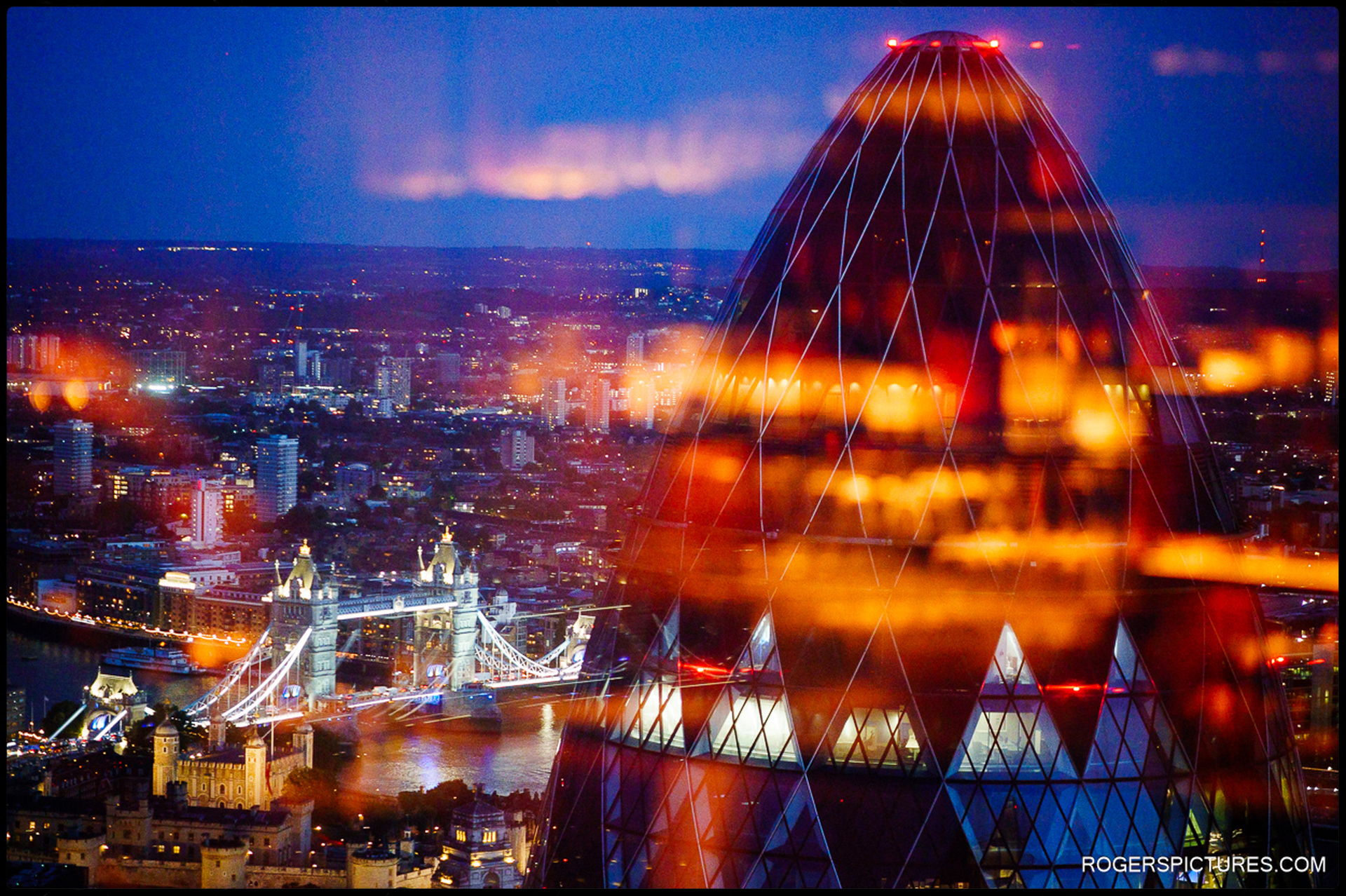 Night-time view of London with Tower Bridge and the River Thames illuminated, photographed through the glass of SushiSamba with reflections of city lights.
