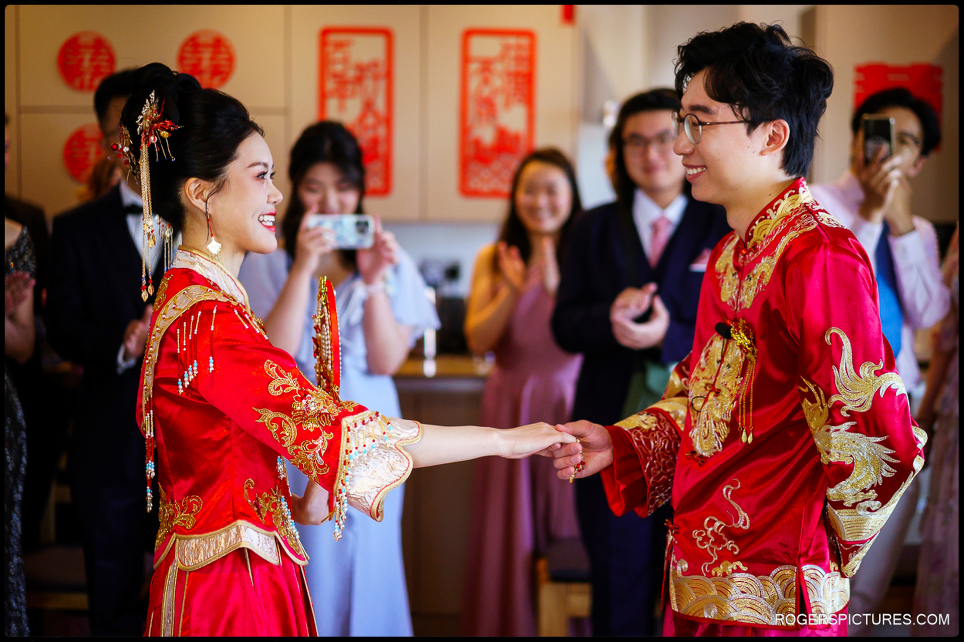 Couple in traditional red Chinese wedding outfits holding hands during the tea ceremony