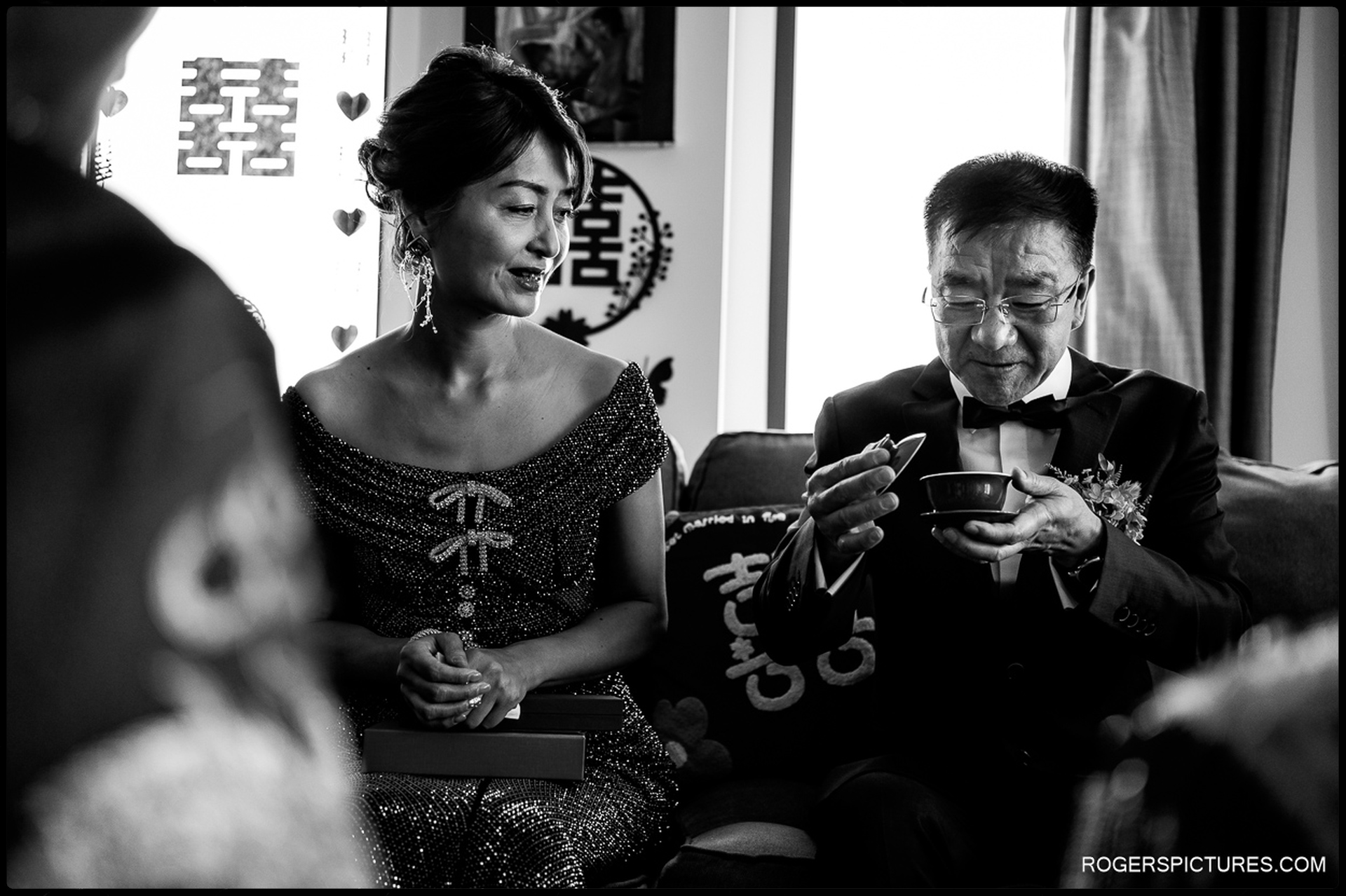 Parents seated together as the father takes tea during the ceremony, shown in black and white
