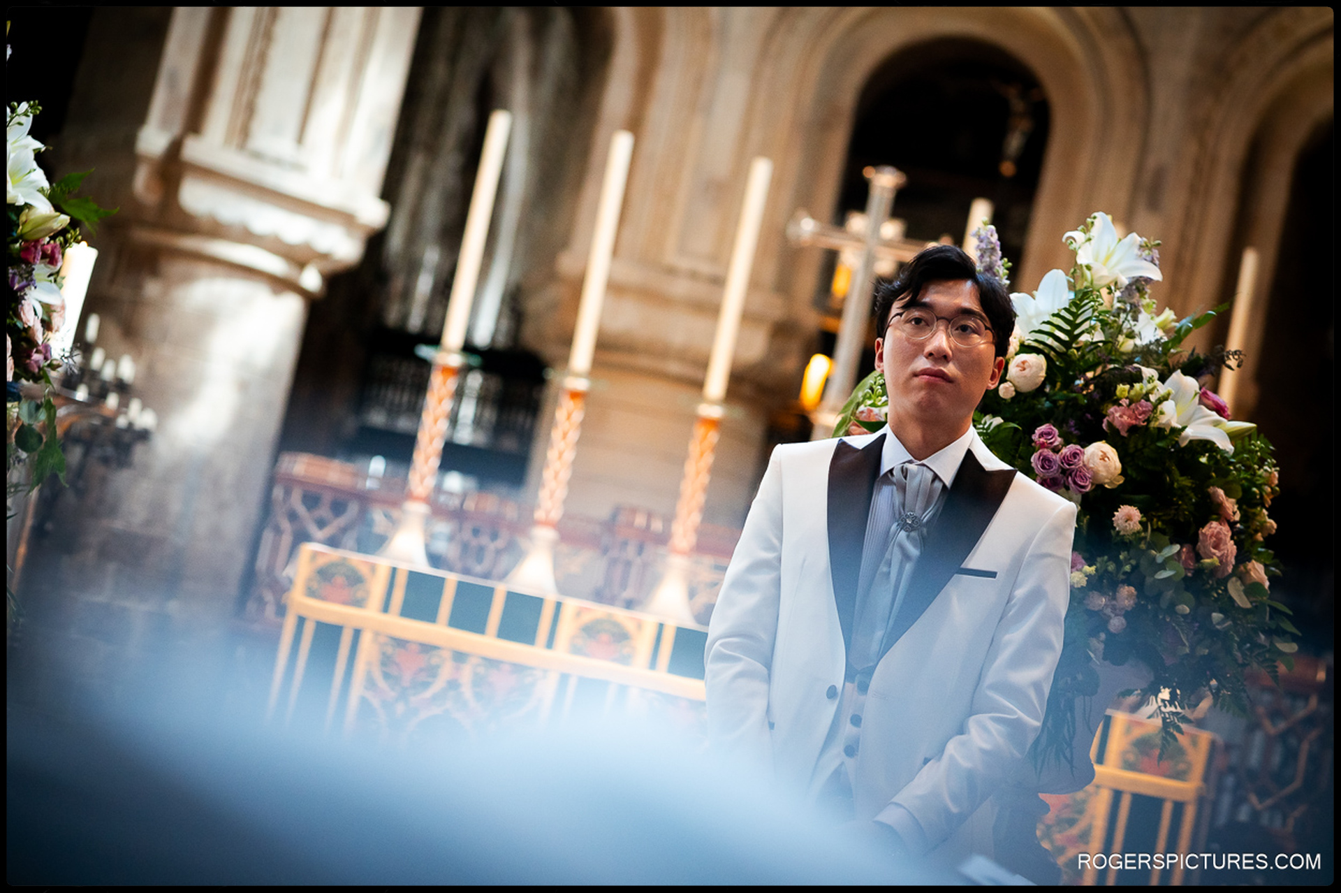 Groom waiting at the front of the church surrounded by flowers and candles