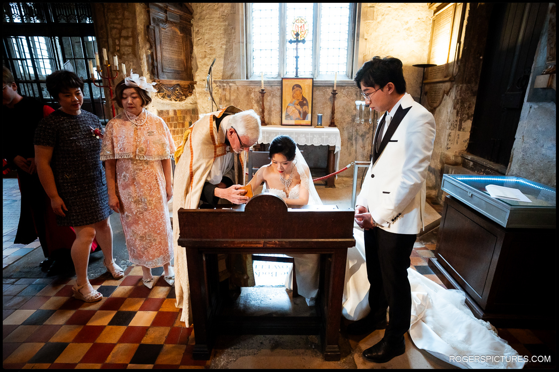 Bride signing the register in the side chapel while guests and the groom watch