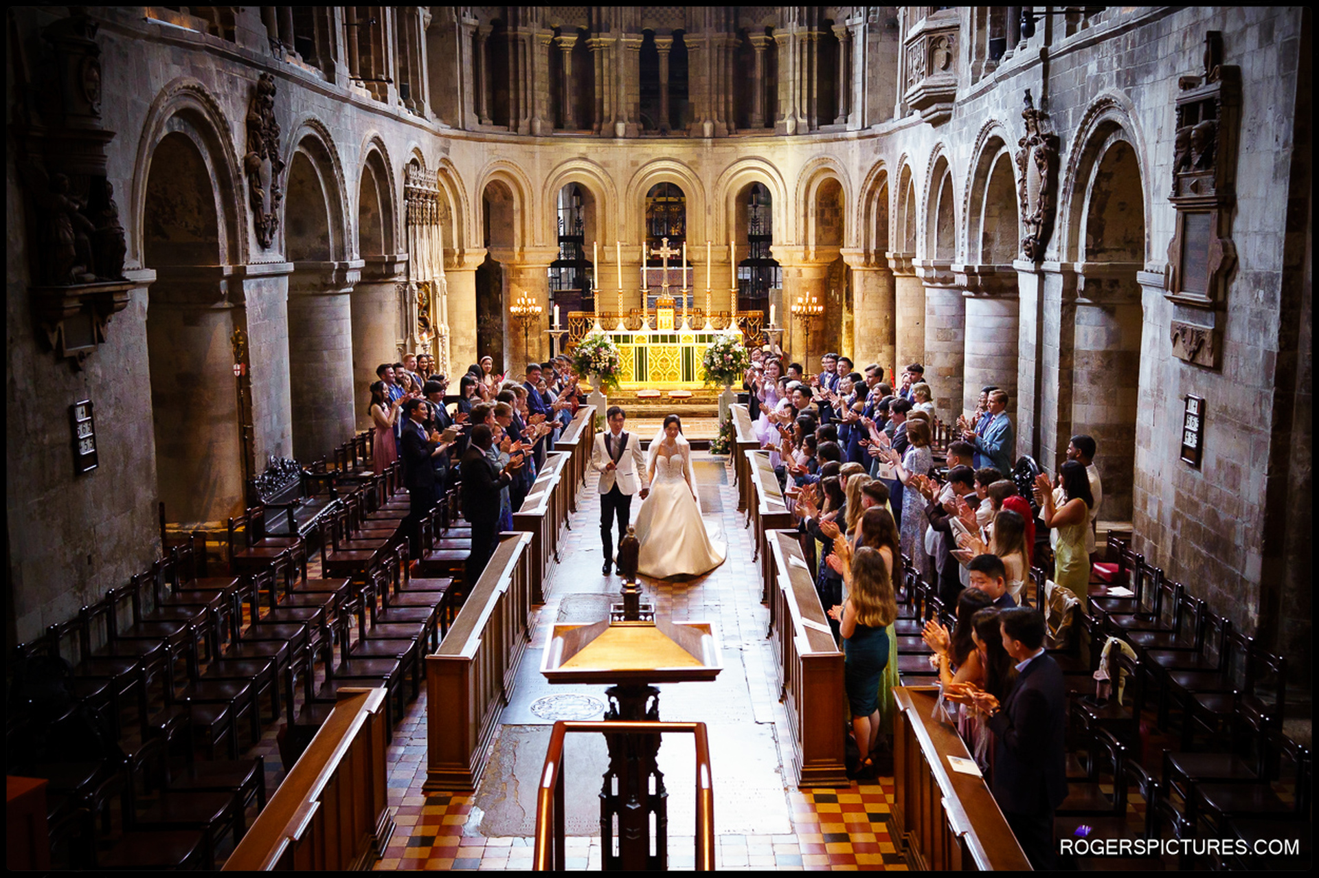 Couple walking back up the aisle as guests applaud inside St Bartholomew the Great