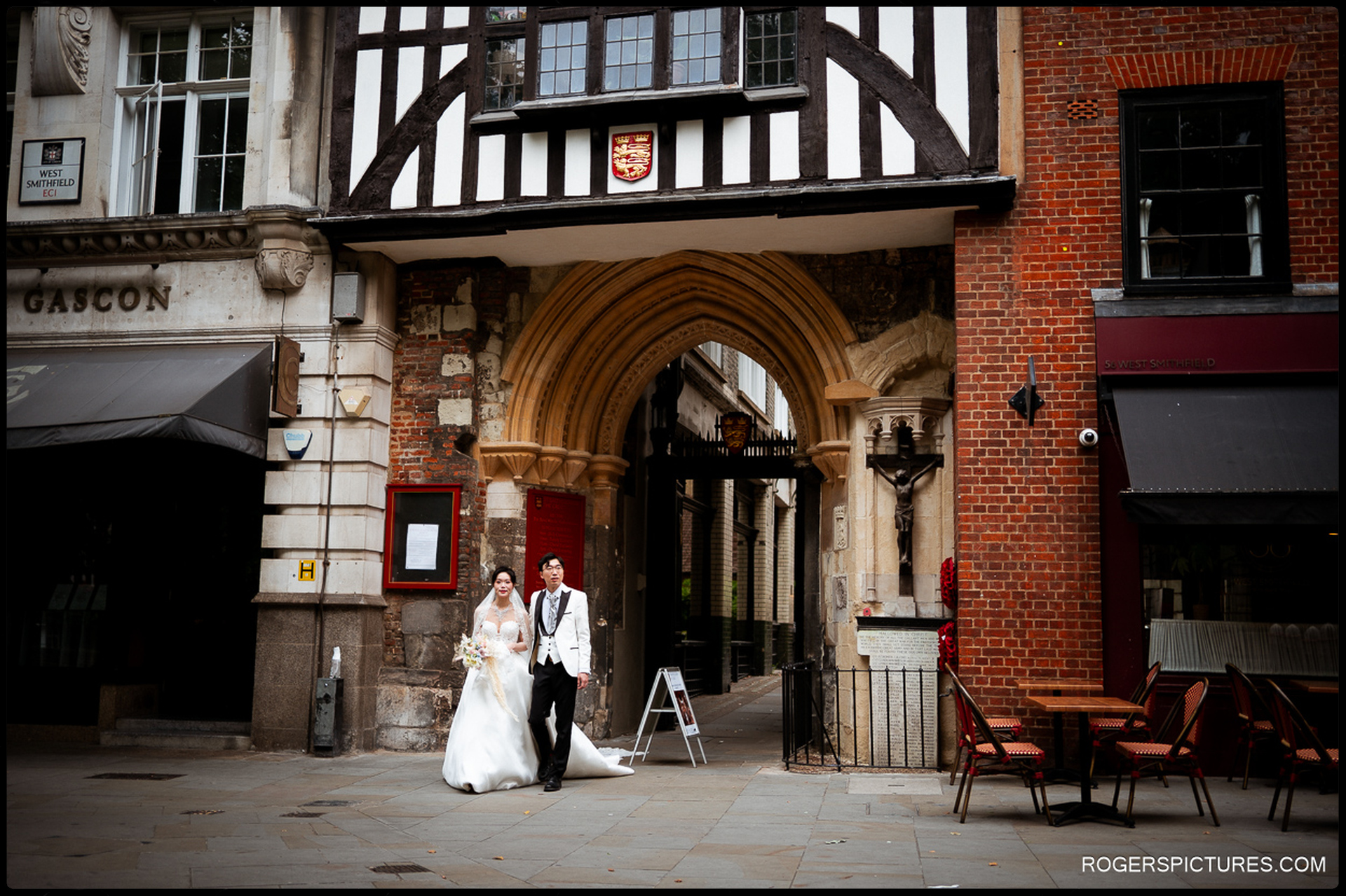 Bride and groom walking together beneath the archway at West Smithfield