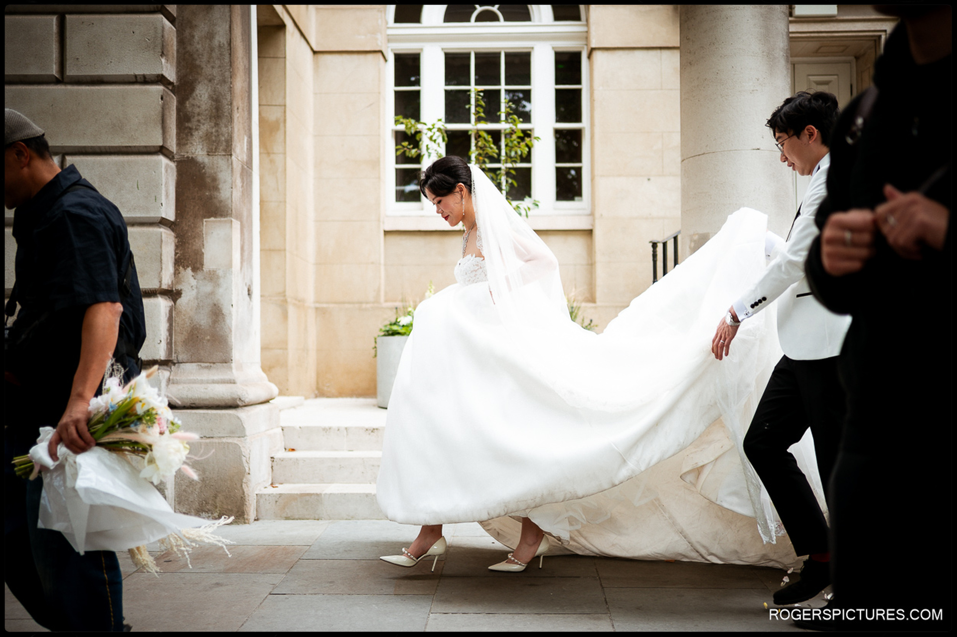 Bride lifting her dress as the groom helps carry the train while walking through Smithfield