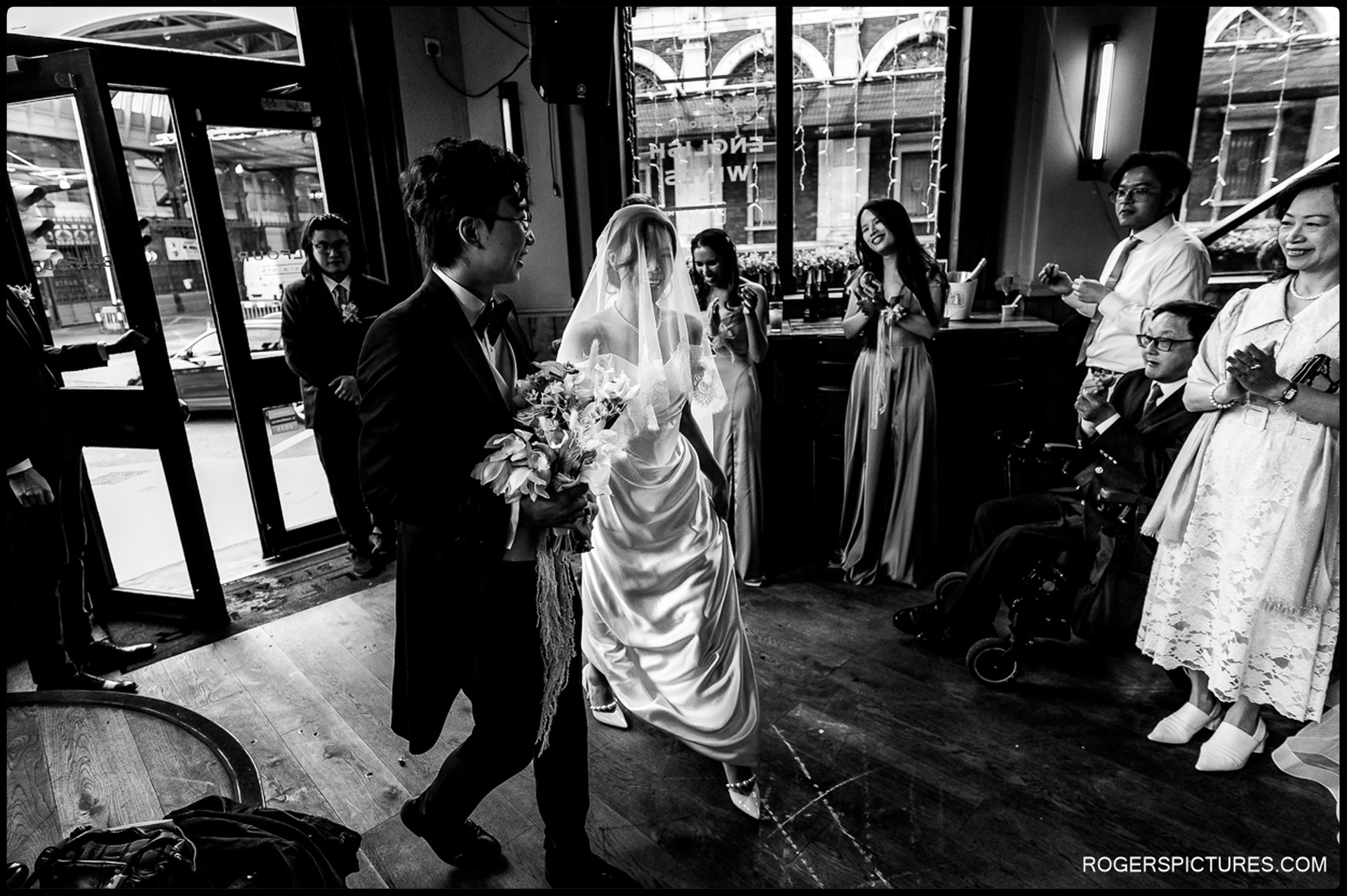 Bride and groom entering the pub reception as guests applaud