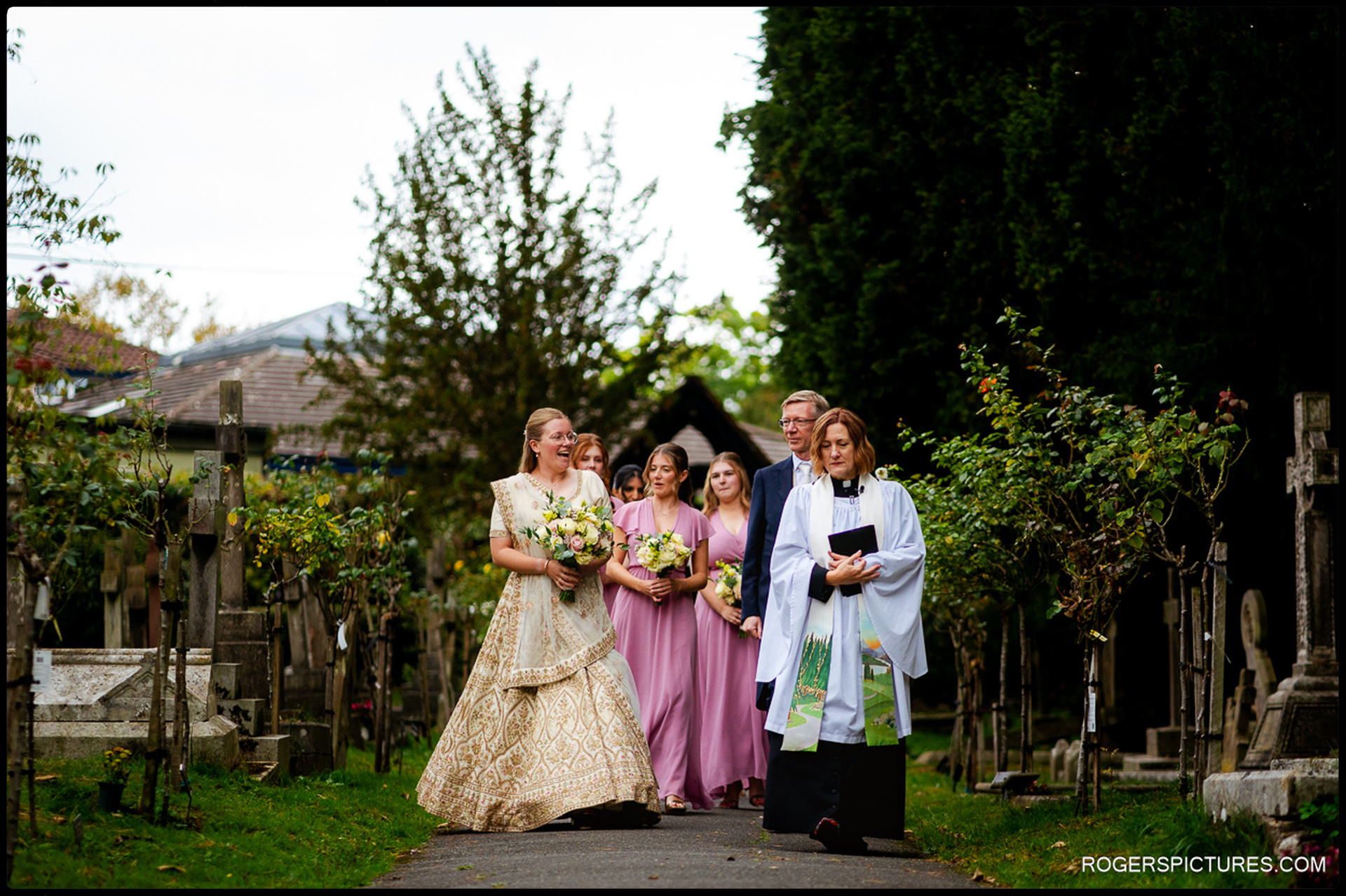 Bride arrives at the churchyard with her father, bridesmaids and the vicar leading the way.