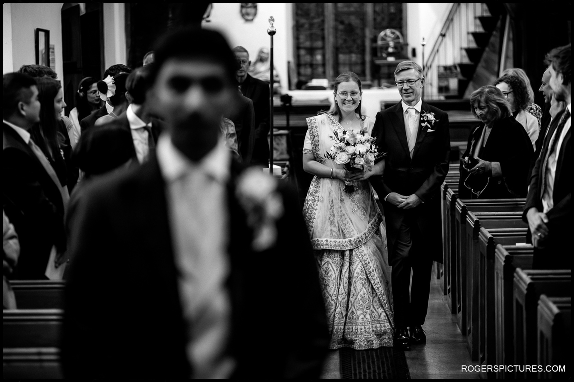 Bride and her father walk up the aisle together as guests watch from the pews.