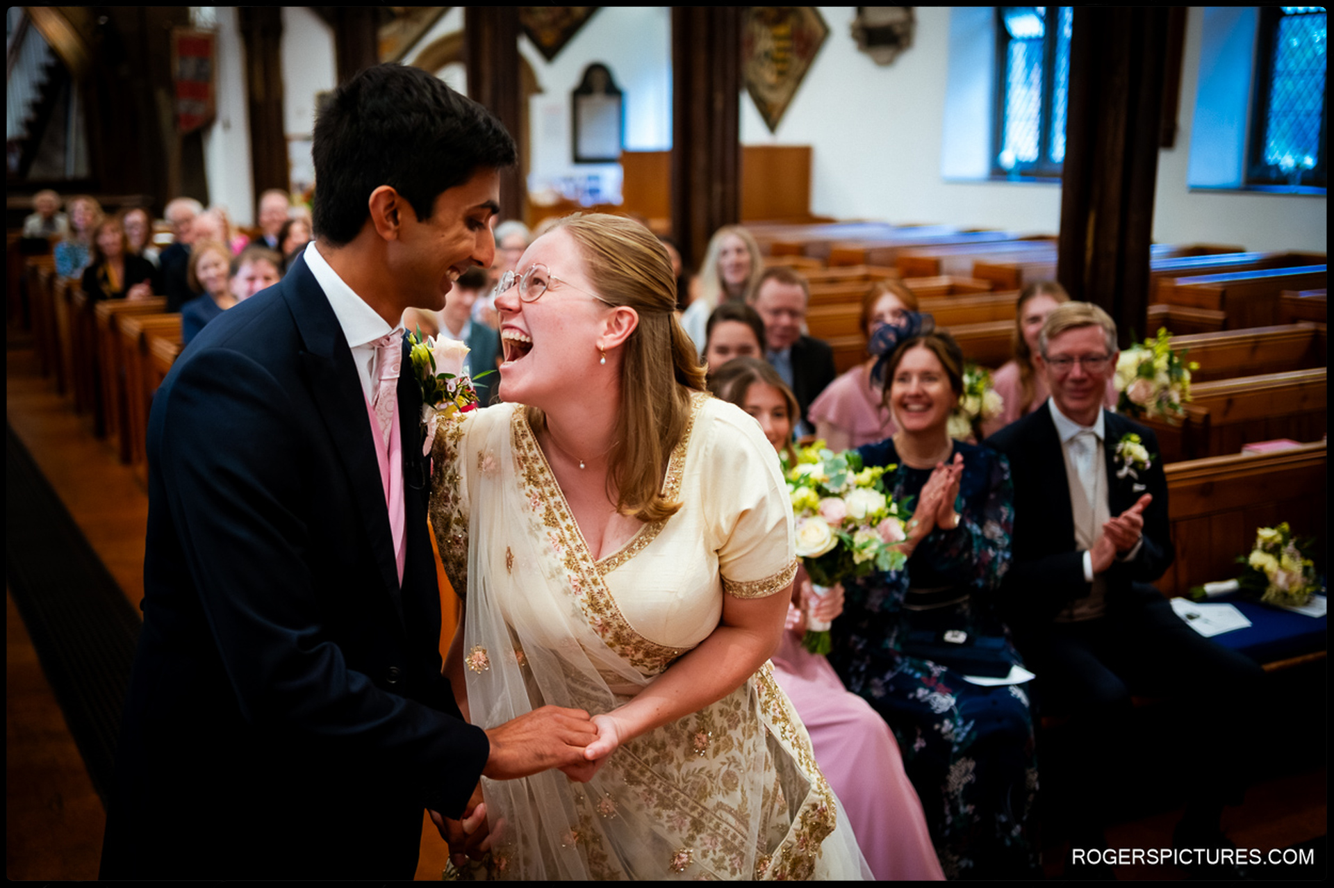 Bride and groom laugh together during the ceremony while guests applaud behind them.