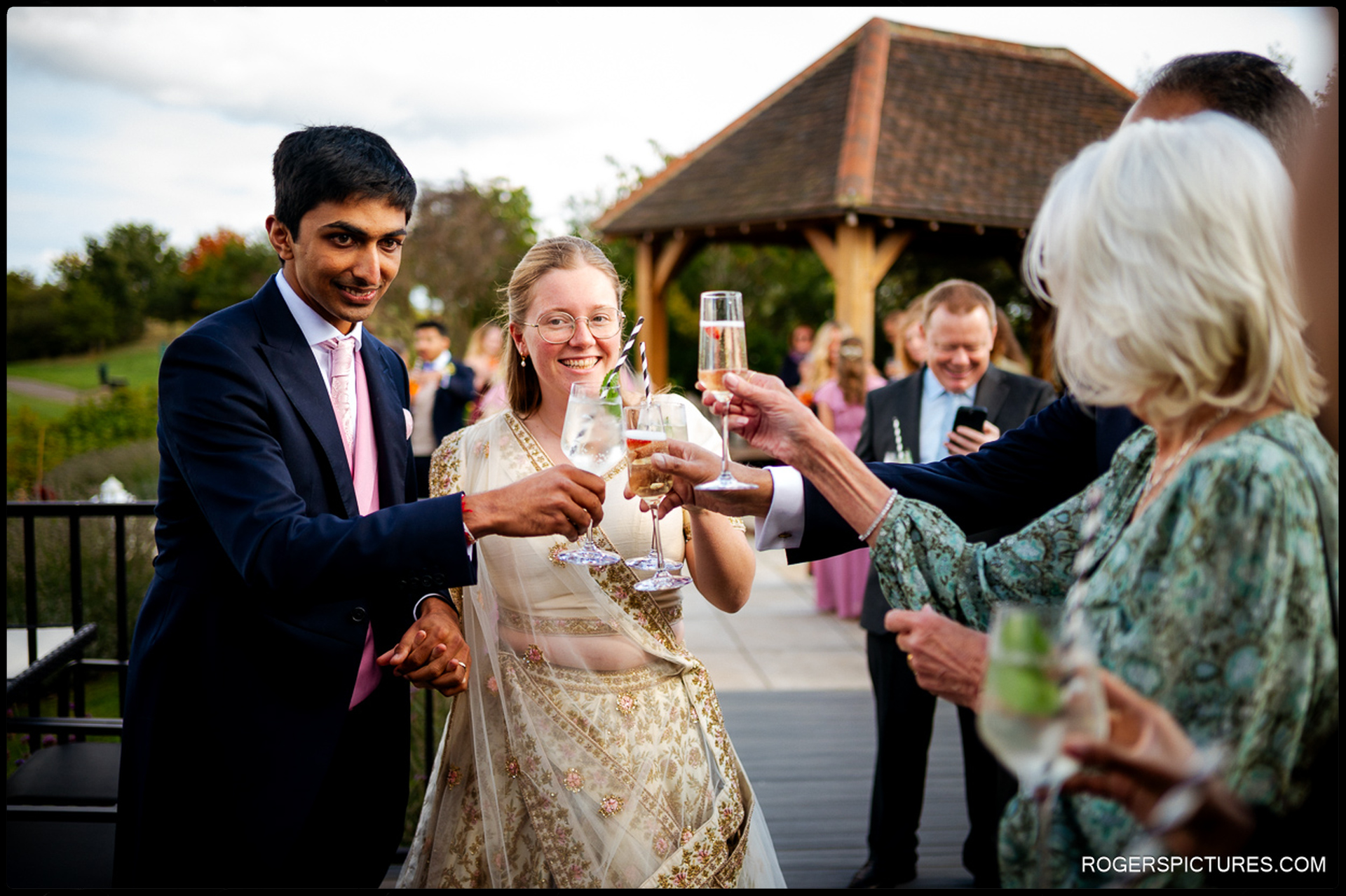Couple raise their glasses in a toast with guests during the outdoor drinks reception.