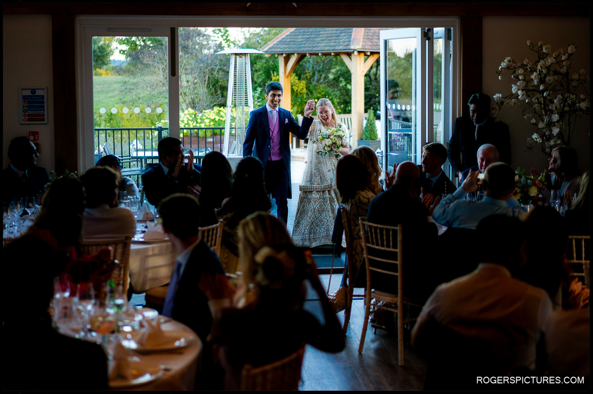 Couple make their entrance to the wedding breakfast as guests applaud inside the reception room.