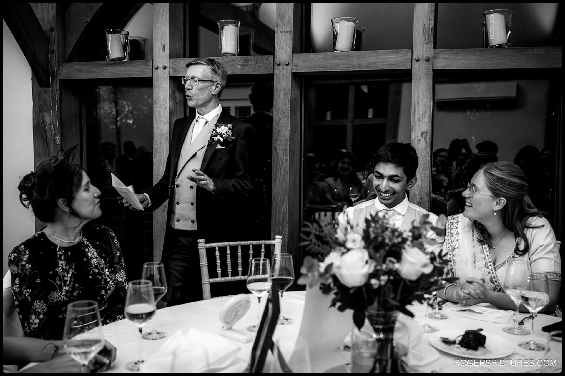 Father of the bride gives his speech while the couple smile and listen at the top table.