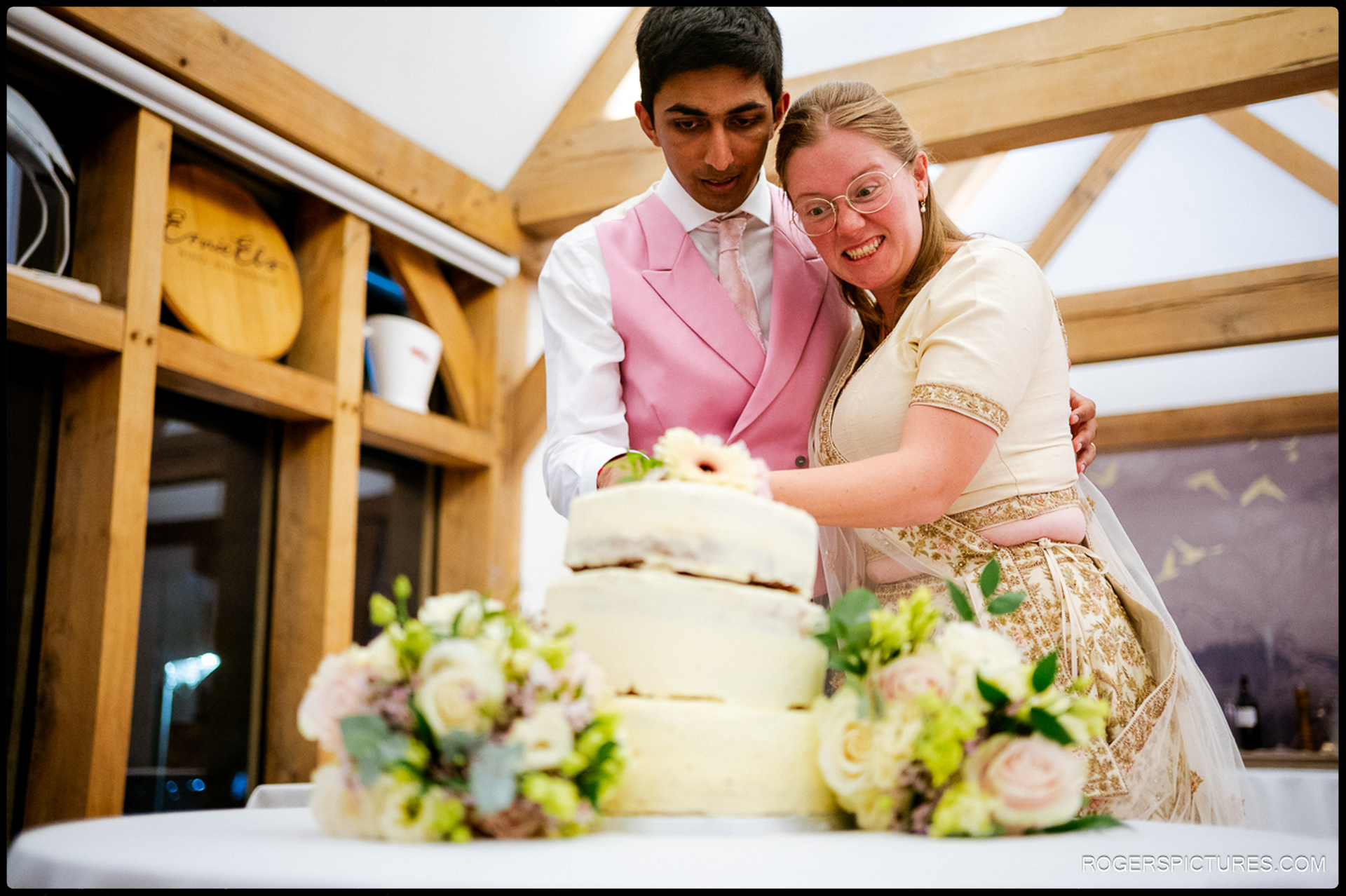 Bride and groom cut their wedding cake together, both smiling as they hold the knife.