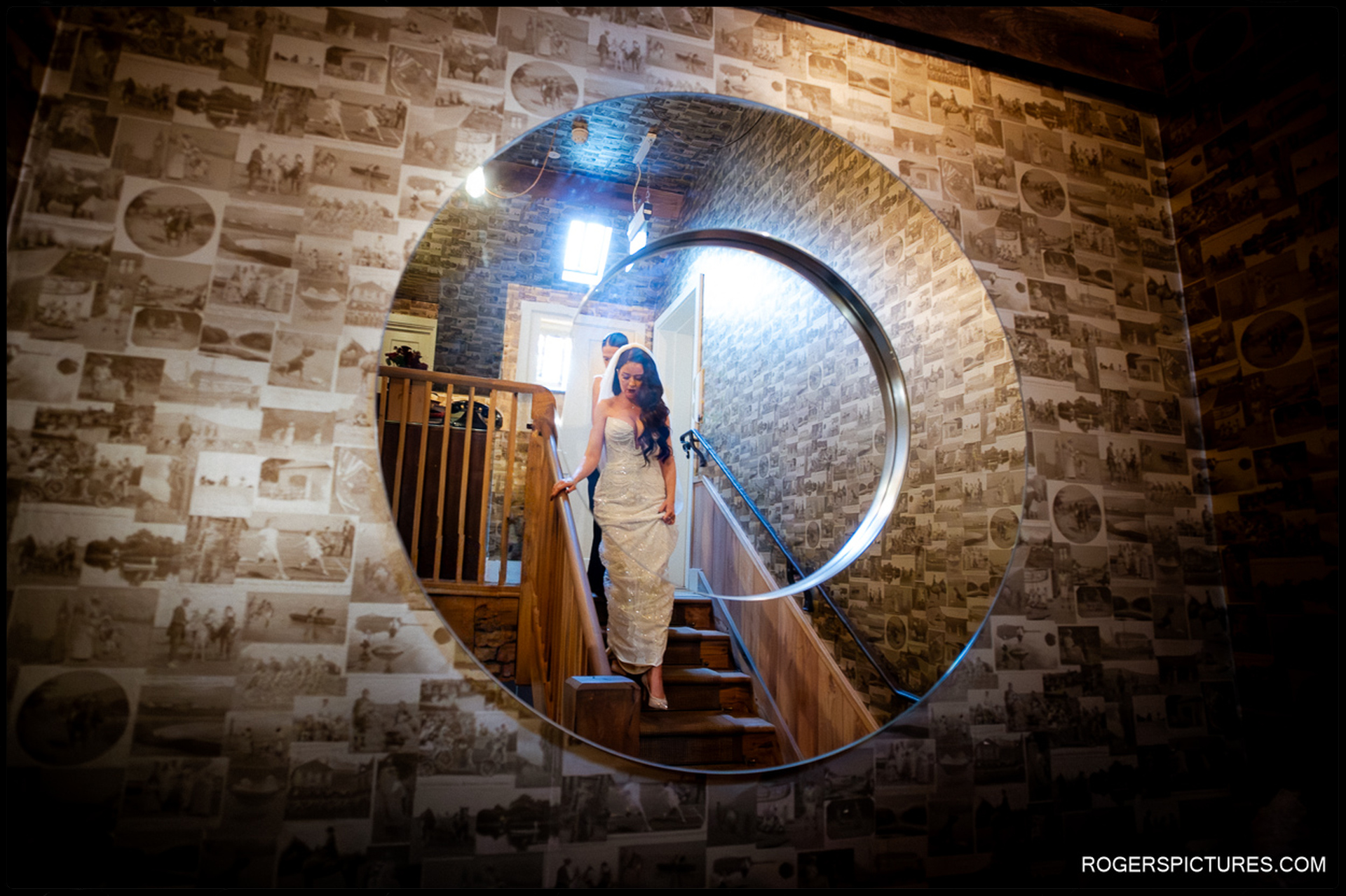 Bride Ciara descending the wooden staircase, reflected in the large, circular photo-collage mirror at The Bell in Ticehurst, just before the ceremony.