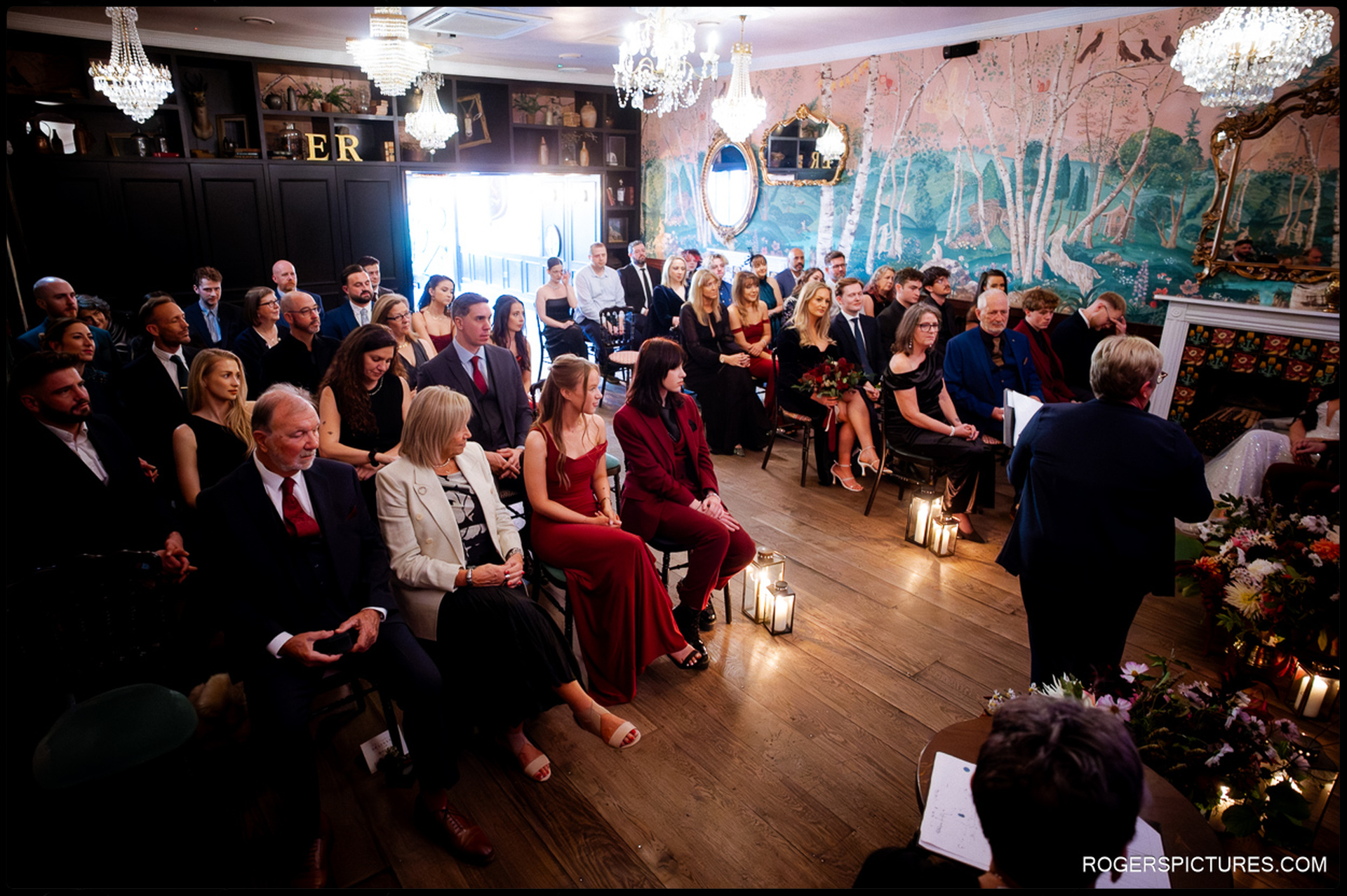Guests seated in the ceremony room at The Bell in Ticehurst, featuring the unique wall mural and chandeliers.