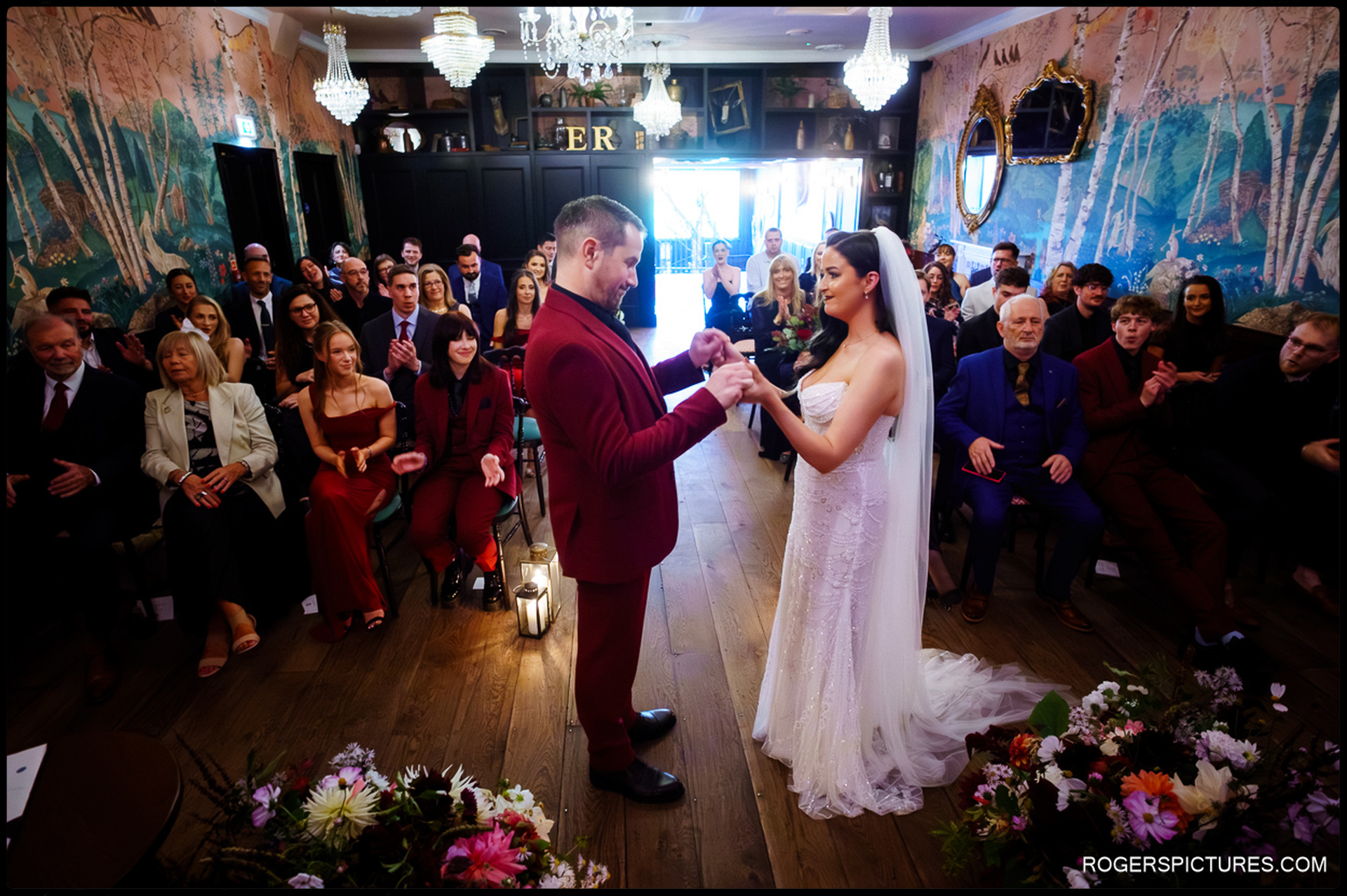 Ciara and Alex standing together, holding hands during their civil marriage ceremony in the uniquely decorated room at The Bell.
