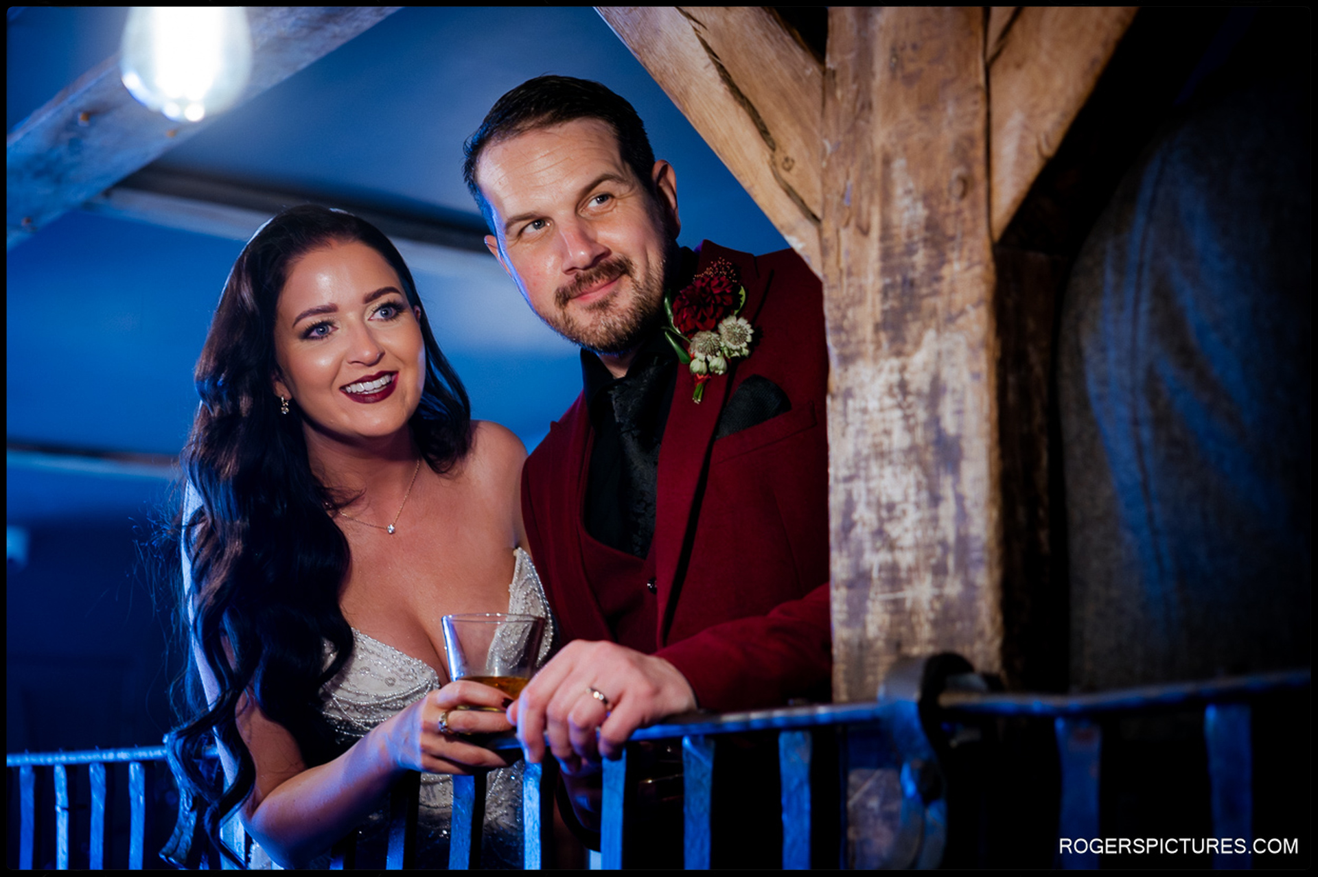 Low-light portrait of the couple on a wooden balcony overlooking the reception, capturing the evening atmosphere.