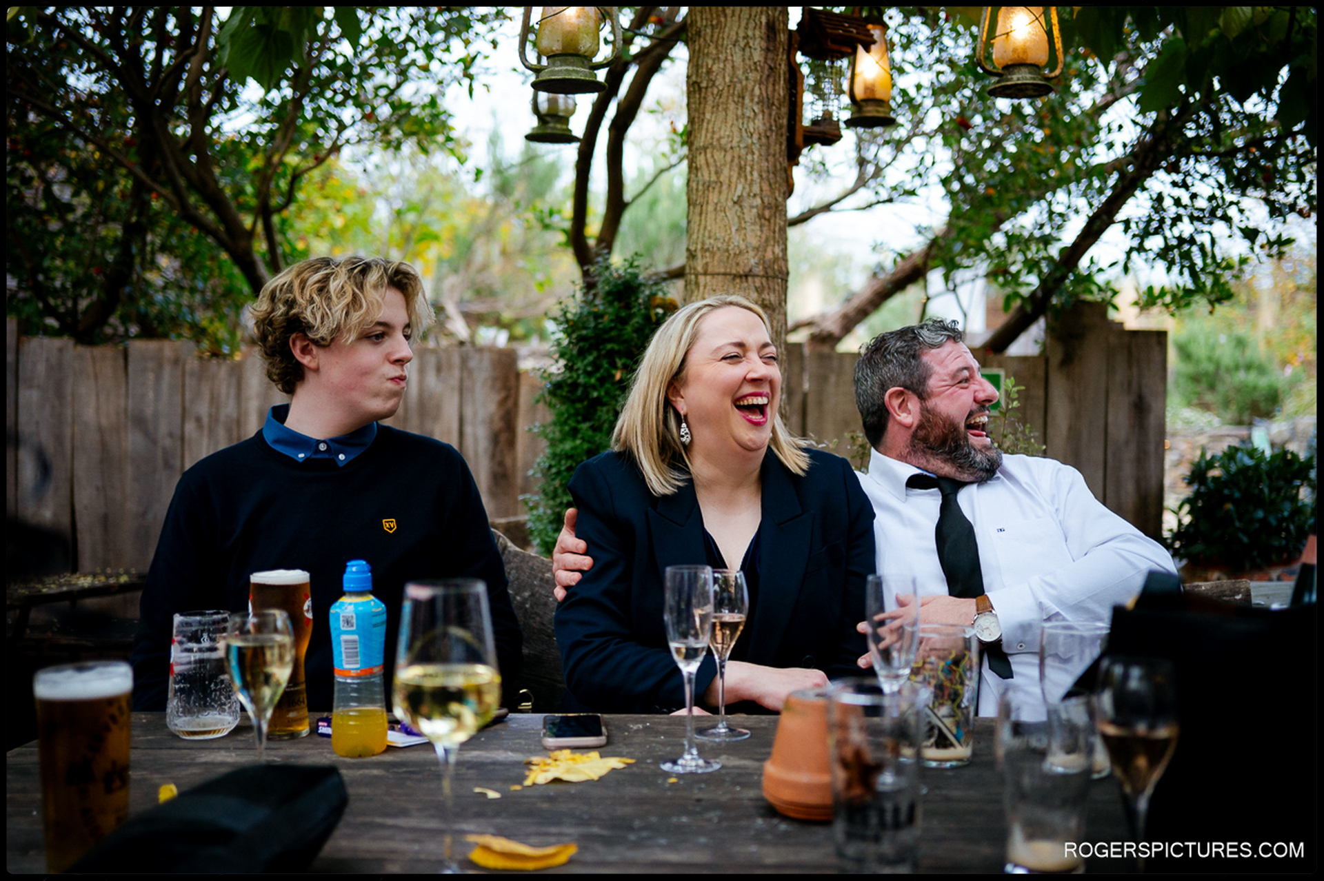 Candid laughter between guests seated outdoors under lanterns during the reception, focusing on natural group interactions.