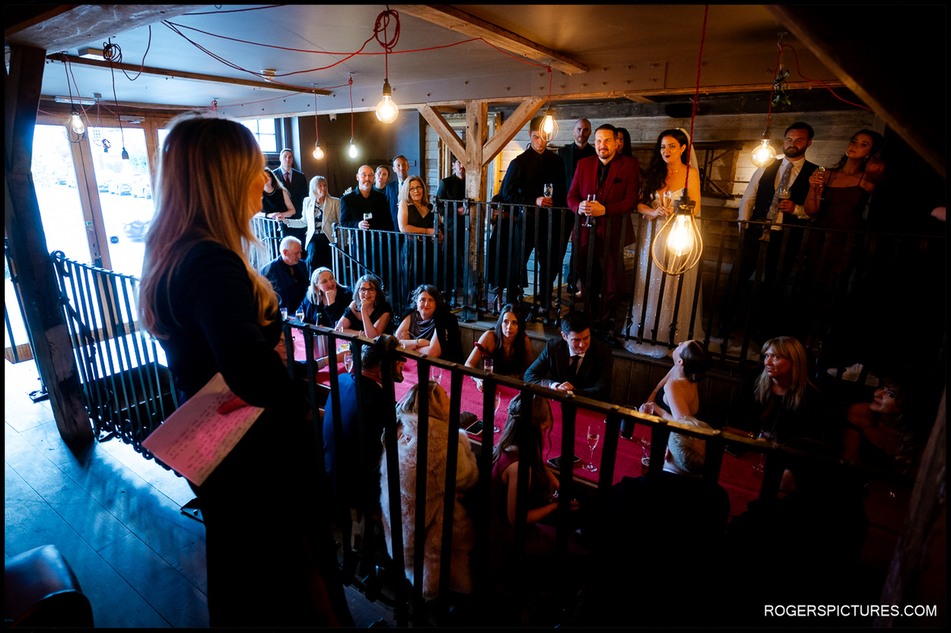 Documentary wide shot of the wedding party gathered across the split-level dining area and mezzanine balcony at The Bell in Ticehurst.