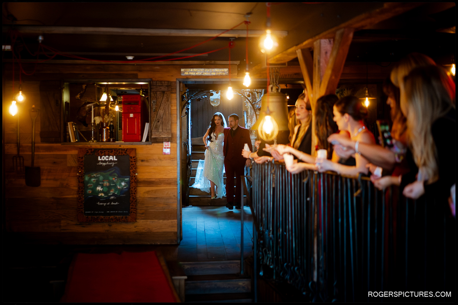 The couple entering the reception space through a wooden archway as guests line the railings to welcome them.
