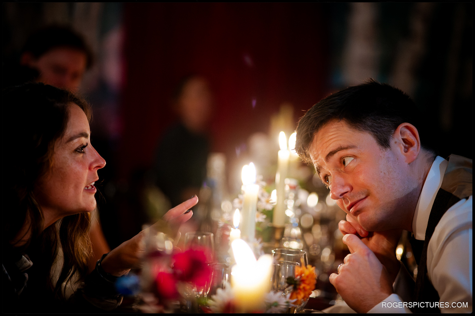 Candid close-up of two guests deeply engaged in conversation at the wedding breakfast table amidst the candlelight.