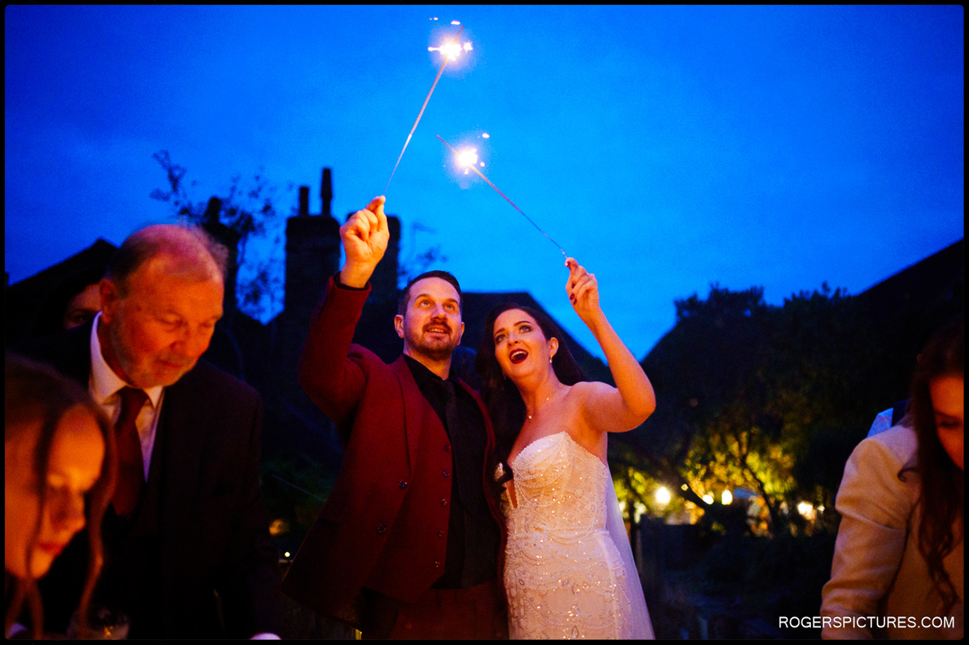 The Bride and Groom holding sparklers aloft against the deep blue twilight sky in the garden.