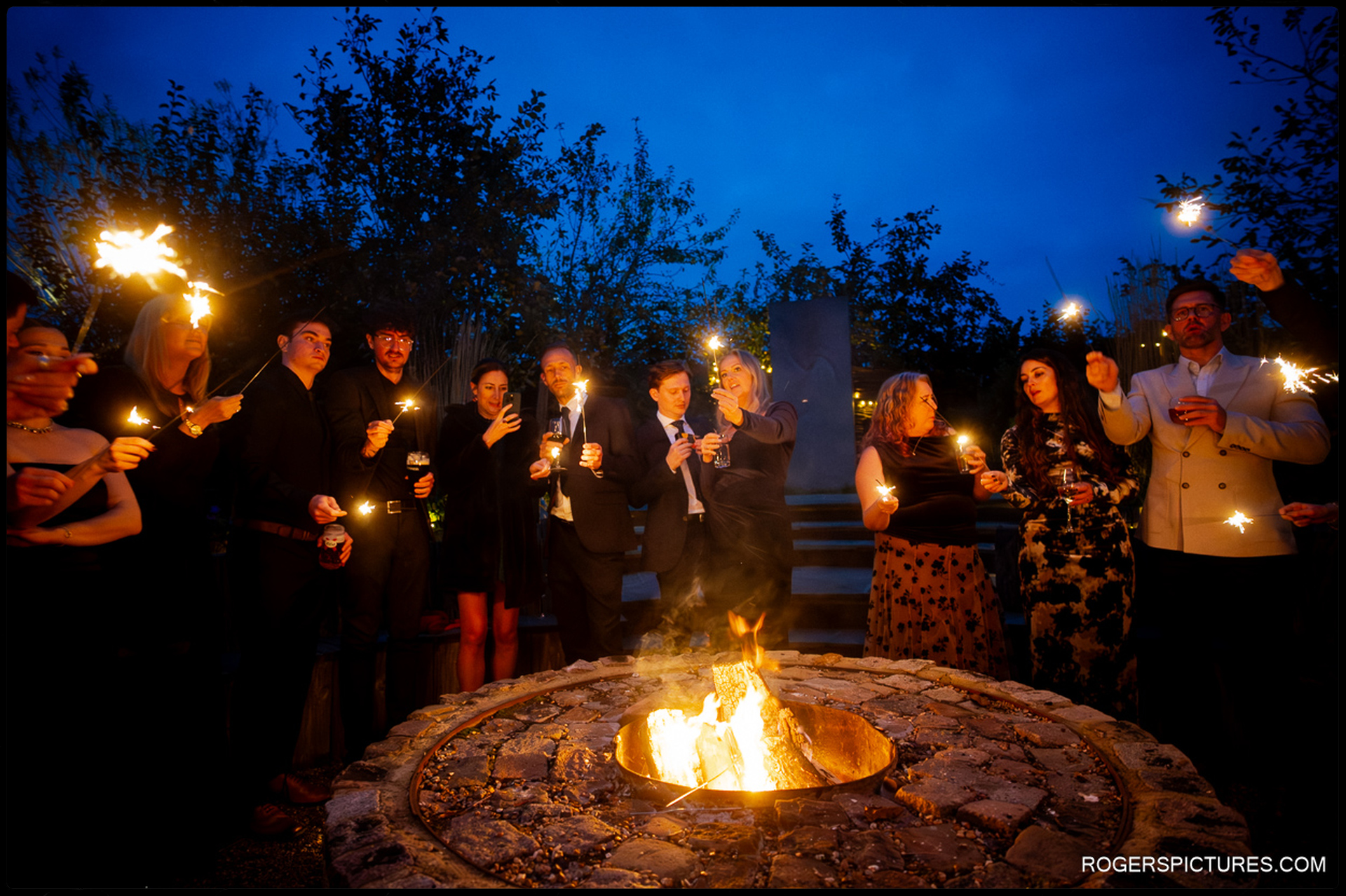 Guests celebrating around the outdoor fire pit with sparklers and drinks, capturing the lively evening reception.