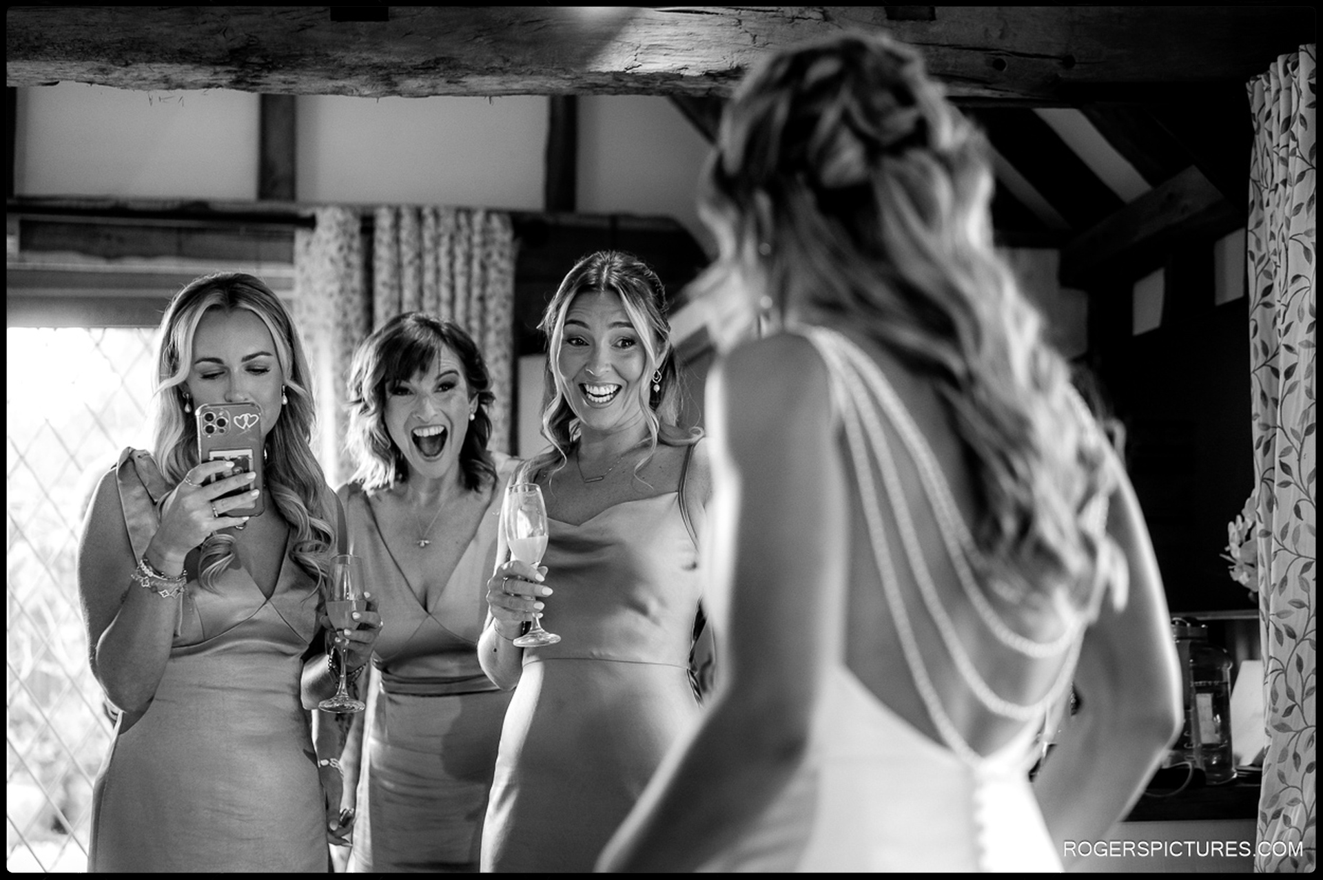 Bridesmaids reacting with joy as the bride shows her wedding dress at Rumbolds Farm.