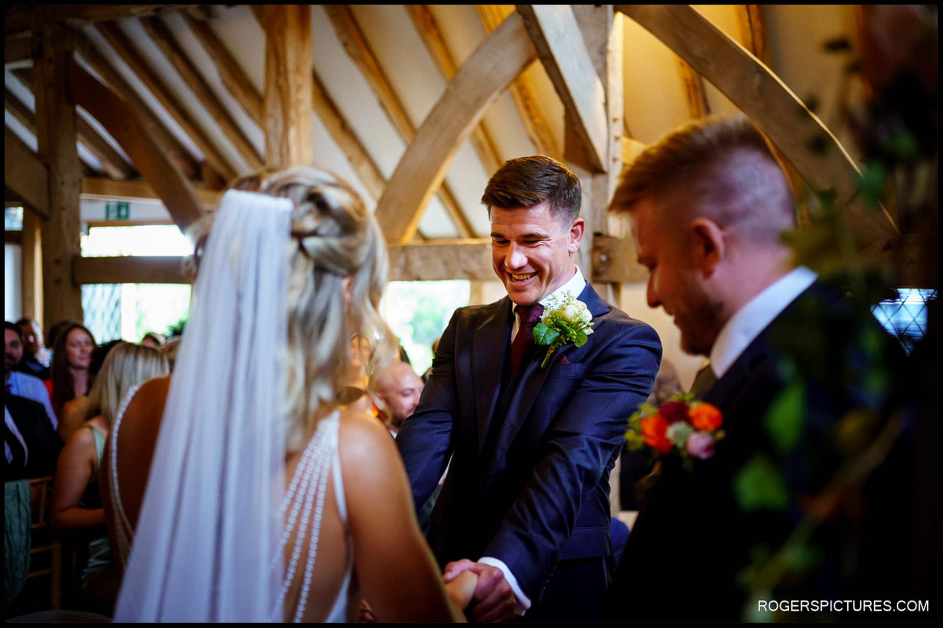 Groom smiling as he holds the bride’s hands during their ceremony at Rumbolds Farm.