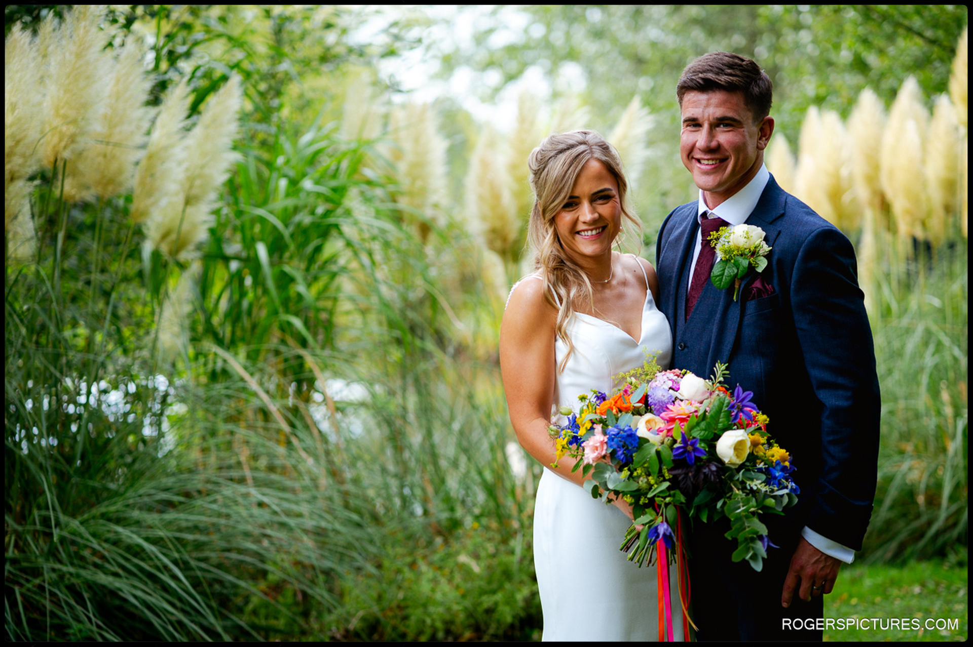 Bride and groom smiling during portraits by the ornamental grasses at Rumbolds Farm.