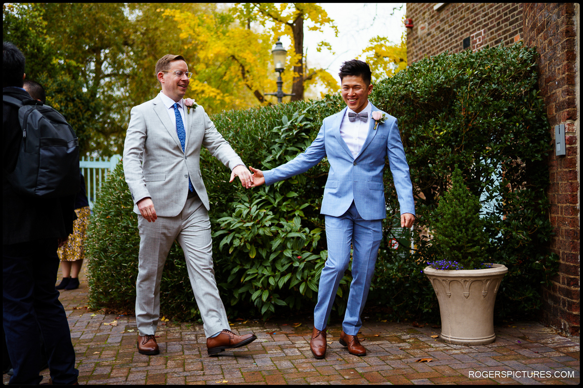 A candid moment of a couple walking hand-in-hand outside Morden Park House with vibrant yellow autumn leaves in the background.
