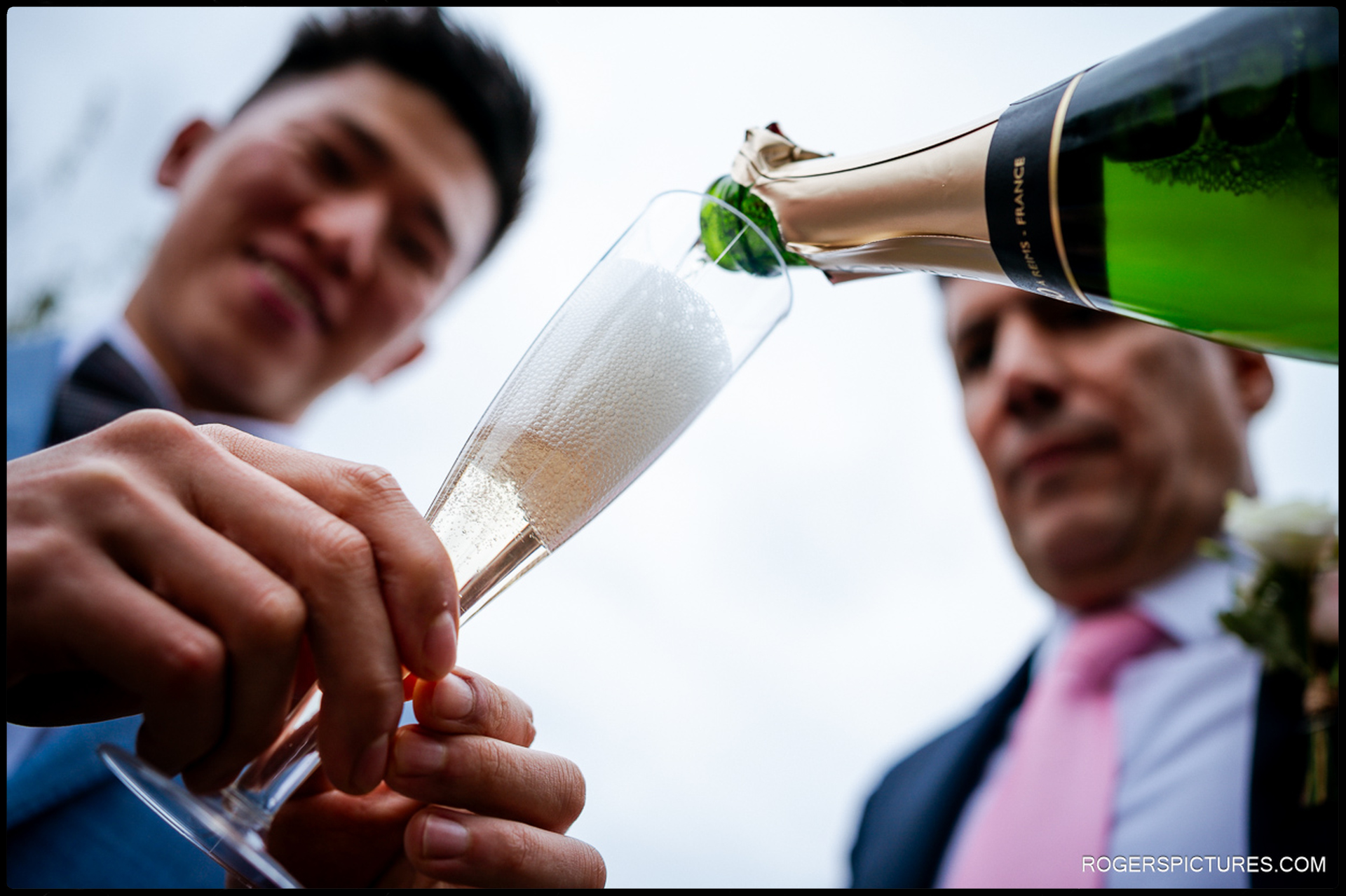 A low-angle, close-up shot of champagne being poured into a flute during the outdoor drinks reception.