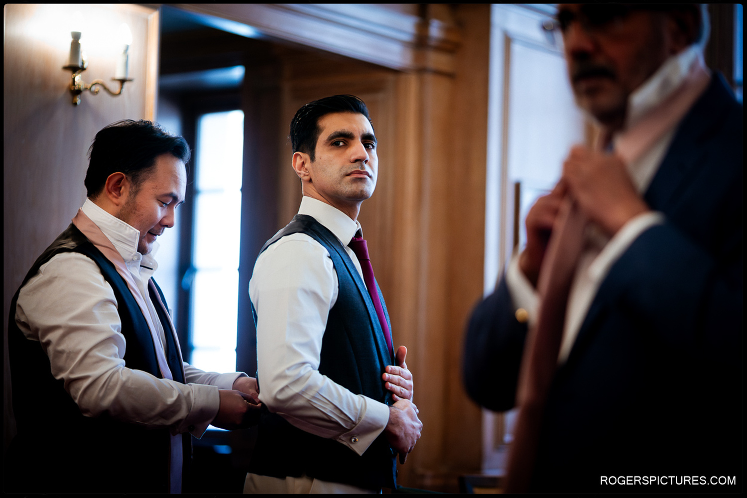 A candid photograph of a groom and his groomsmen adjusting their waistcoats and ties during morning preparations in a wood-panelled room at 113 Chancery Lane.
