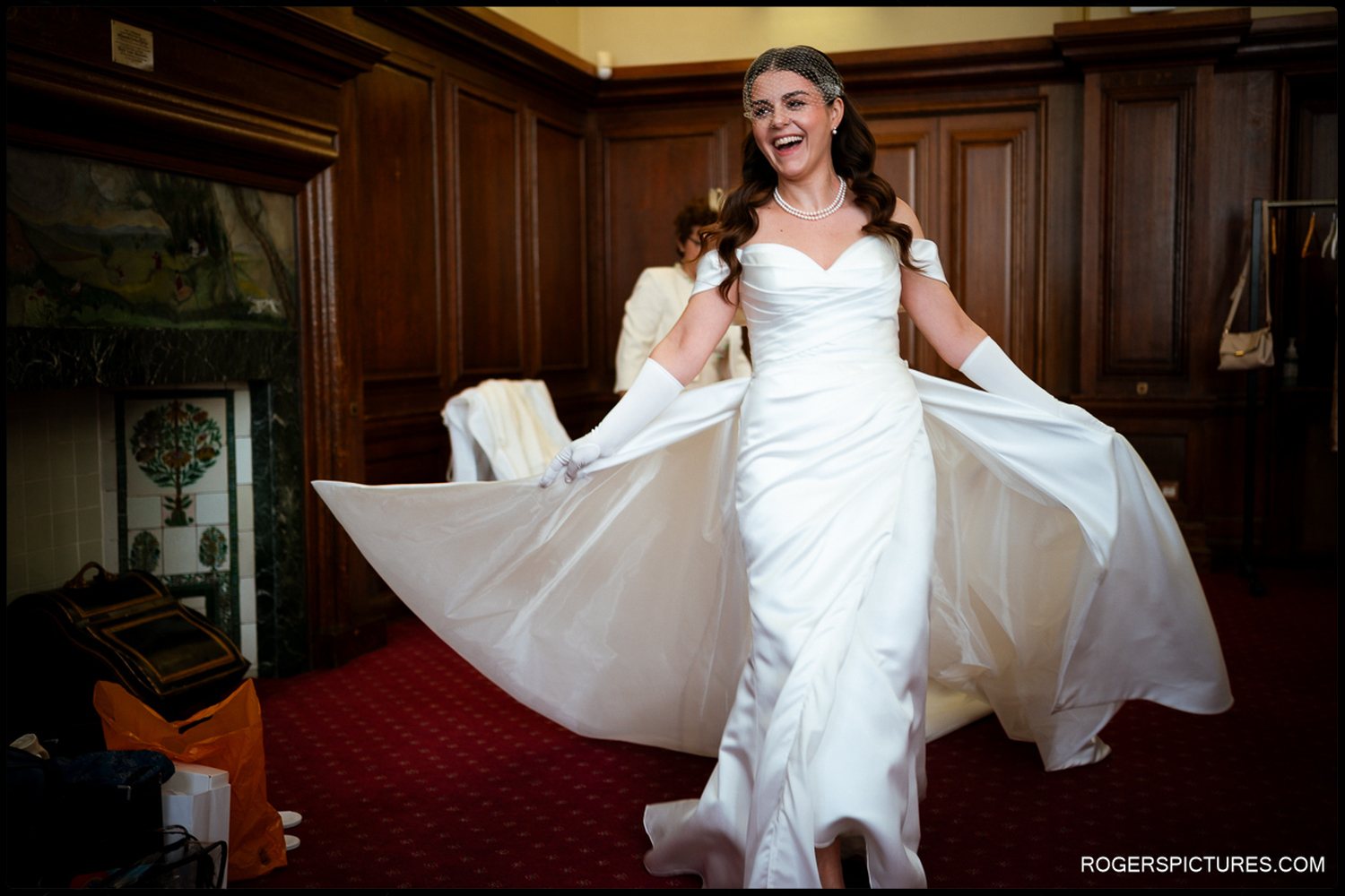 A candid shot of a bride laughing and holding out the skirts of her wedding dress in an elegant wood-panelled suite at The Law Society.