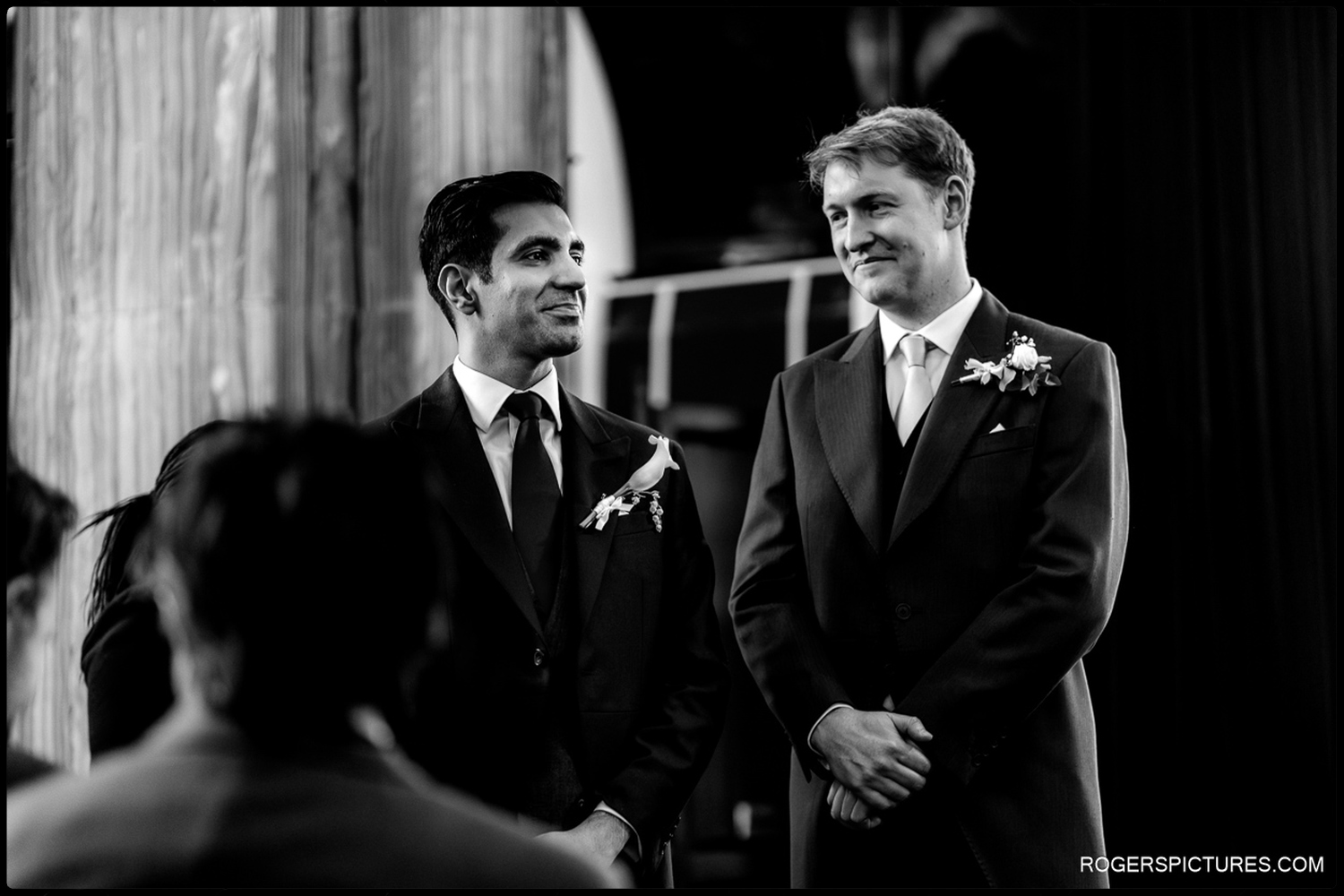 A black and white natural moment showing a groom and his best man sharing a quiet smile during the wedding ceremony at 113 Chancery Lane.