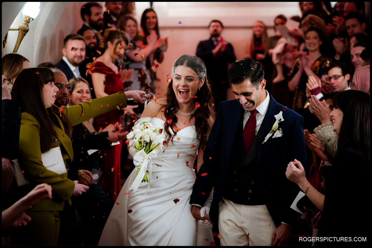 A joyful, candid shot of a bride laughing with excitement as she and her groom descend a staircase showered in colourful confetti.