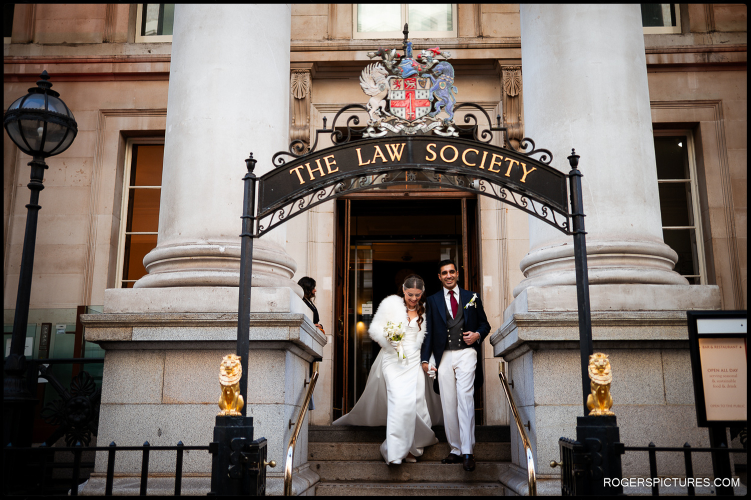 A natural moment of a newlyweds walking out of the main entrance of The Law Society under the historic arched signage at 113 Chancery Lane.
