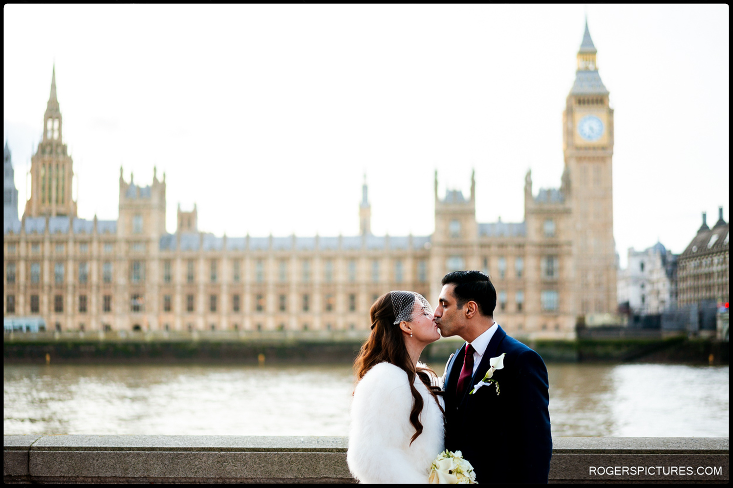 A natural portrait of a bride and groom sharing a kiss on the South Bank with the Houses of Parliament and Big Ben as a backdrop during their winter wedding.